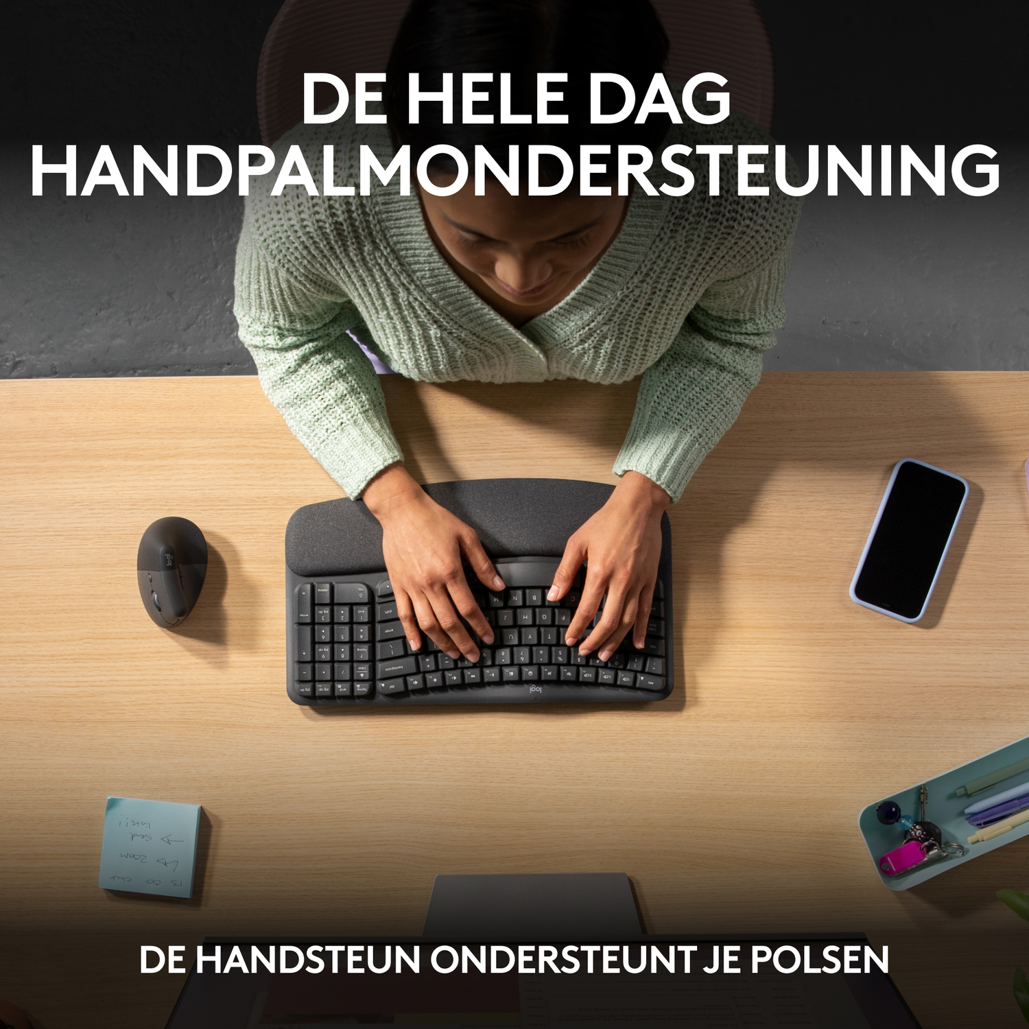 Osoba pisząca na klawiaturze z podpórką pod nadgarstki. Mysz i telefon są na biurku.