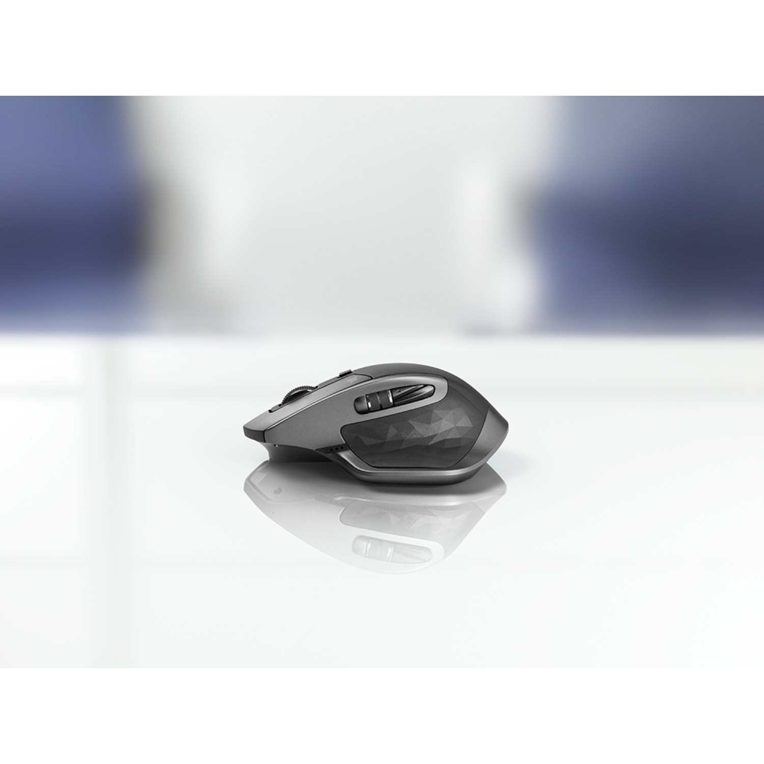 Szara mysz bezprzewodowa na białej powierzchni. Tło jest rozmyte, białe i niebieskie.