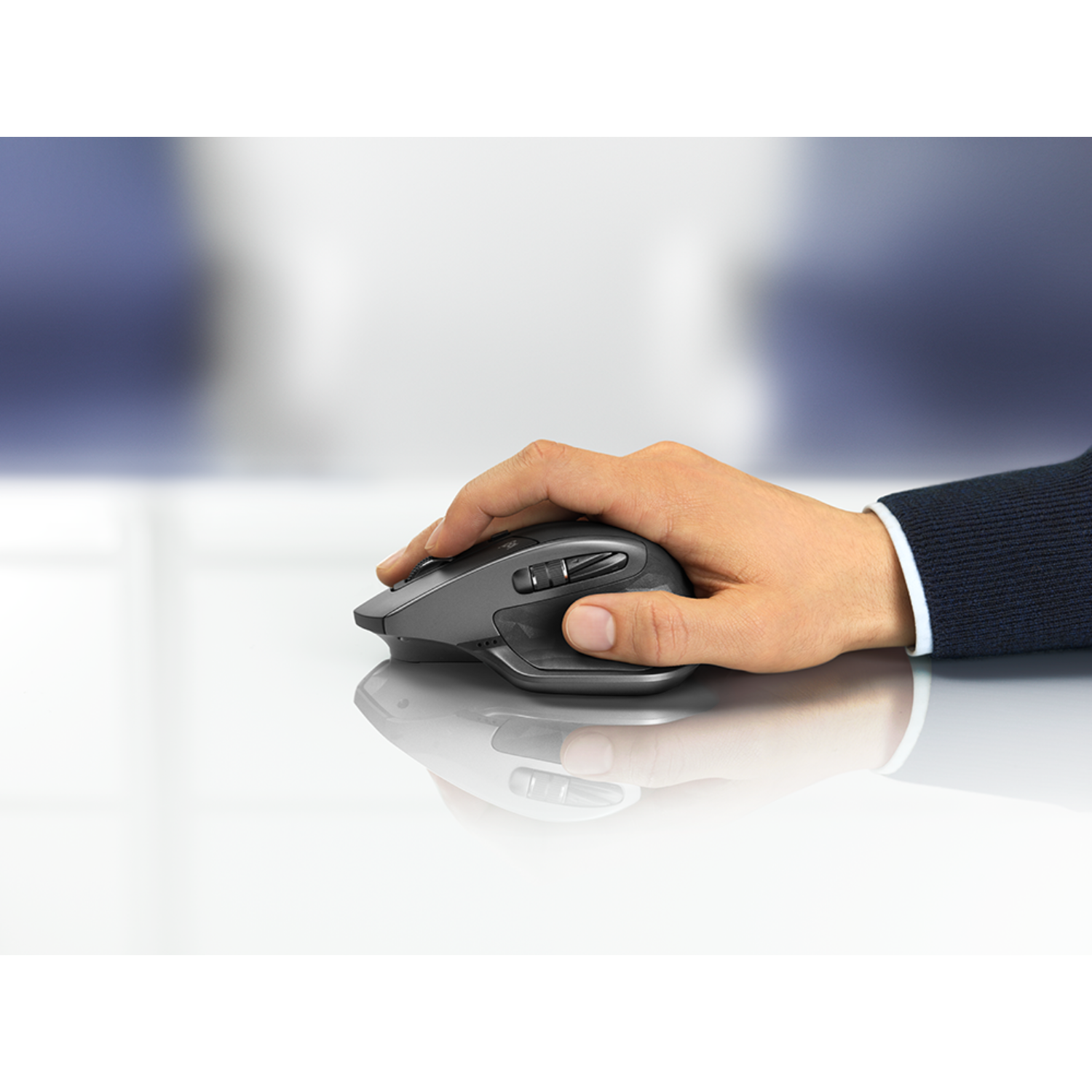 Dłoń trzymająca szarą i czarną mysz komputerową na białej powierzchni.