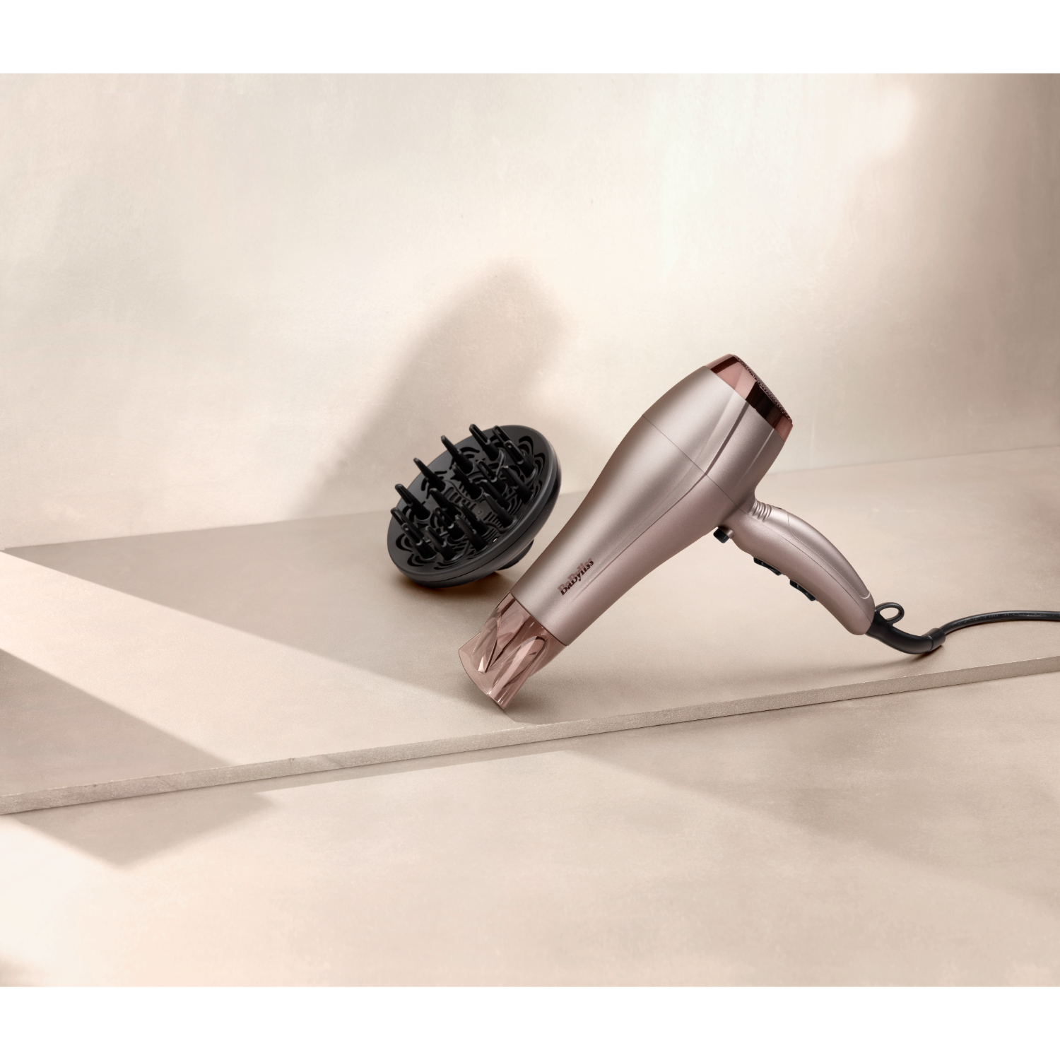 Un asciugacapelli e un diffusore sono posizionati su una superficie beige, con uno sfondo neutro.