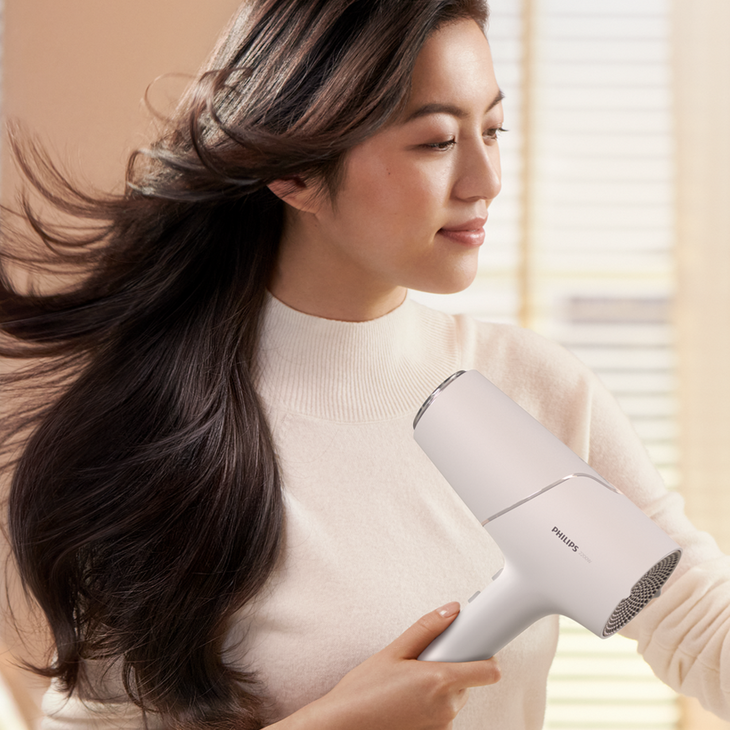 Kobieta trzymająca białą suszarkę do włosów, suszy swoje ciemnobrązowe włosy.