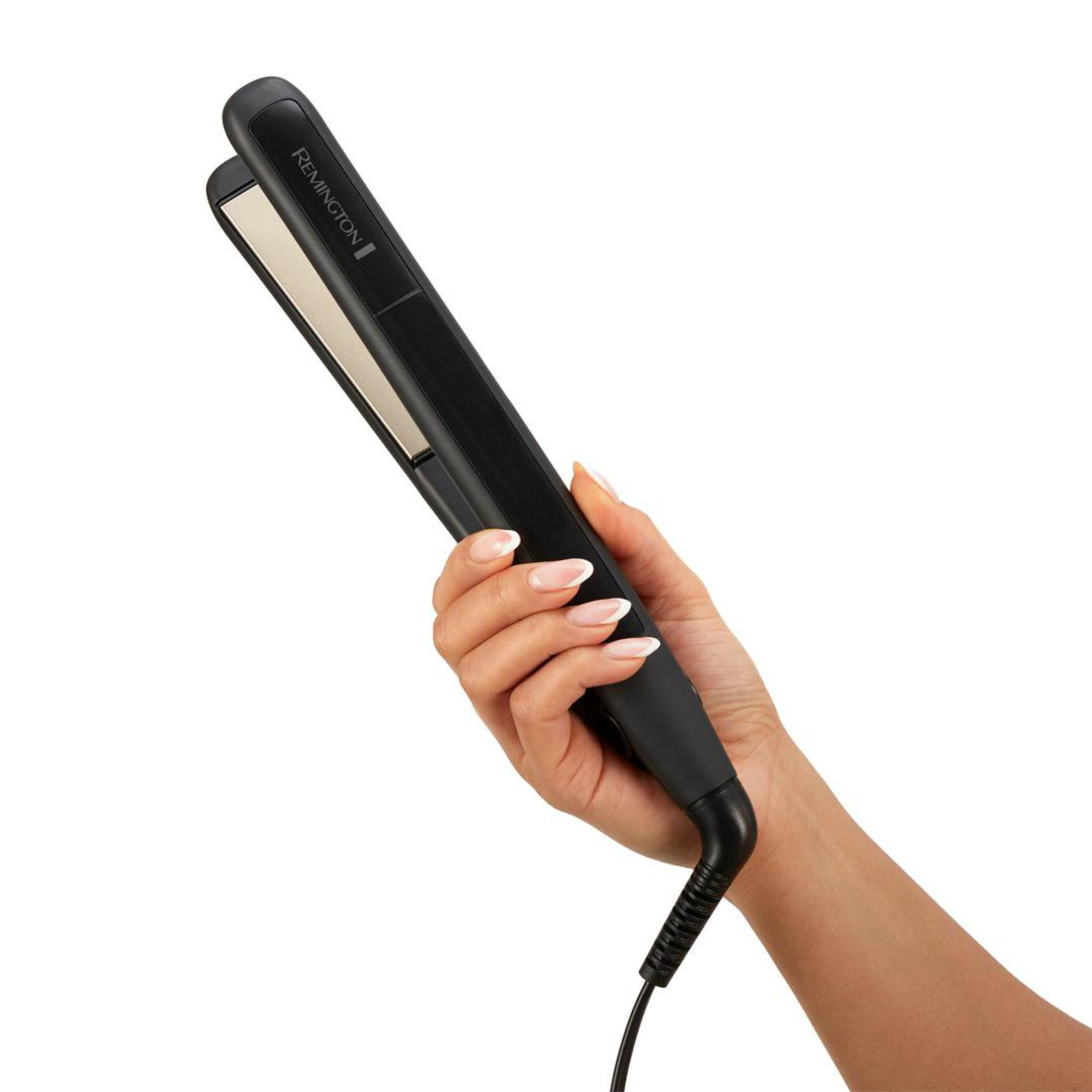 Eine Hand einer Frau, die einen schwarzen Remington-Haarglätter hält, isoliert vor weißem Hintergrund.