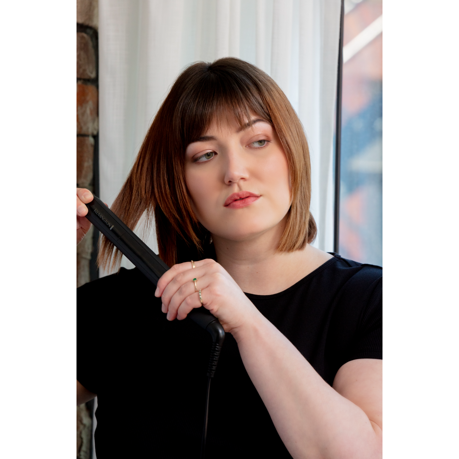 Frau, die ihr braunes Haar mit einem schwarzen Haarglätter glättet.