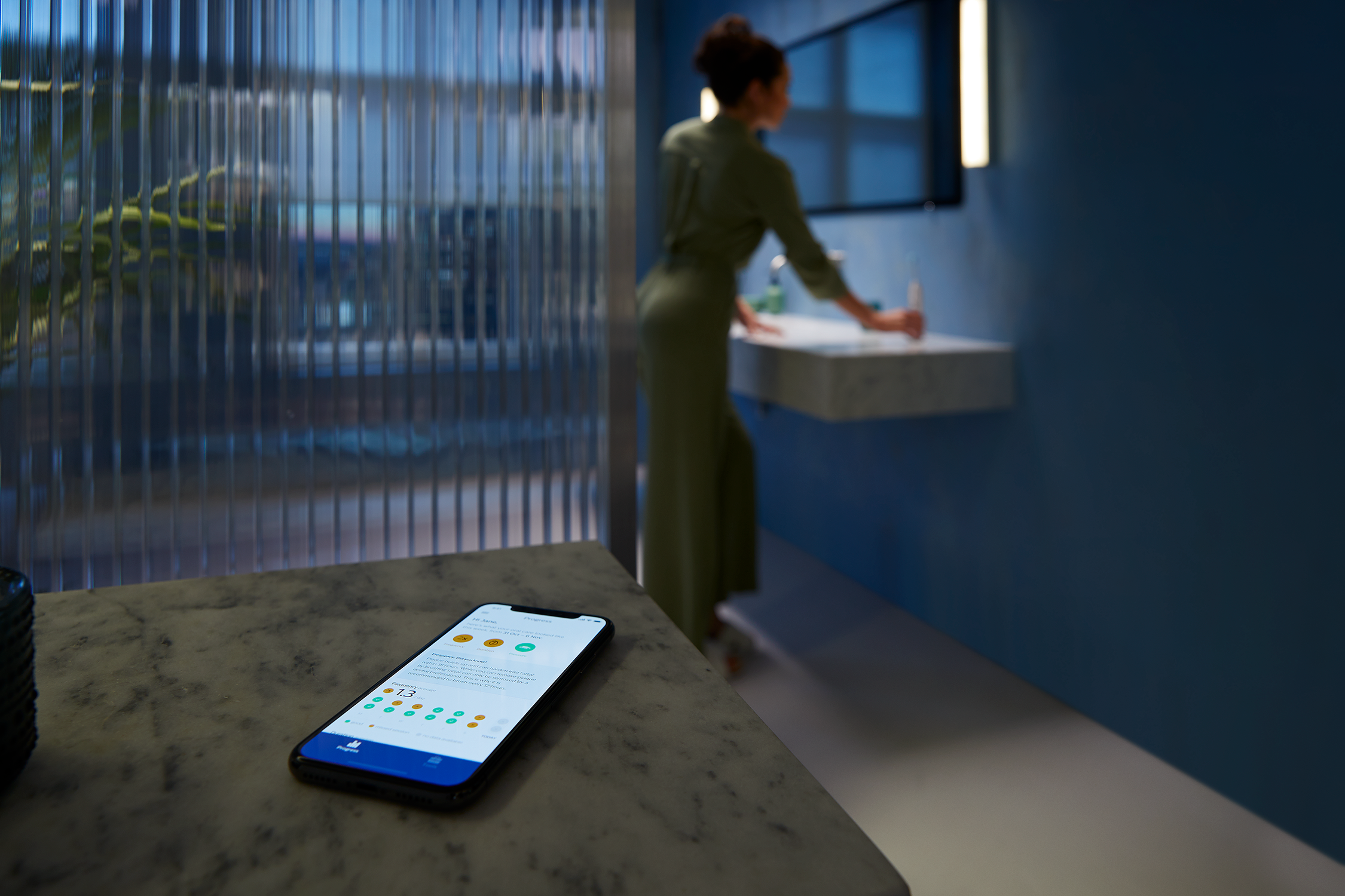 Teléfono mostrando datos de la aplicación en un mostrador, mujer cepillándose los dientes.