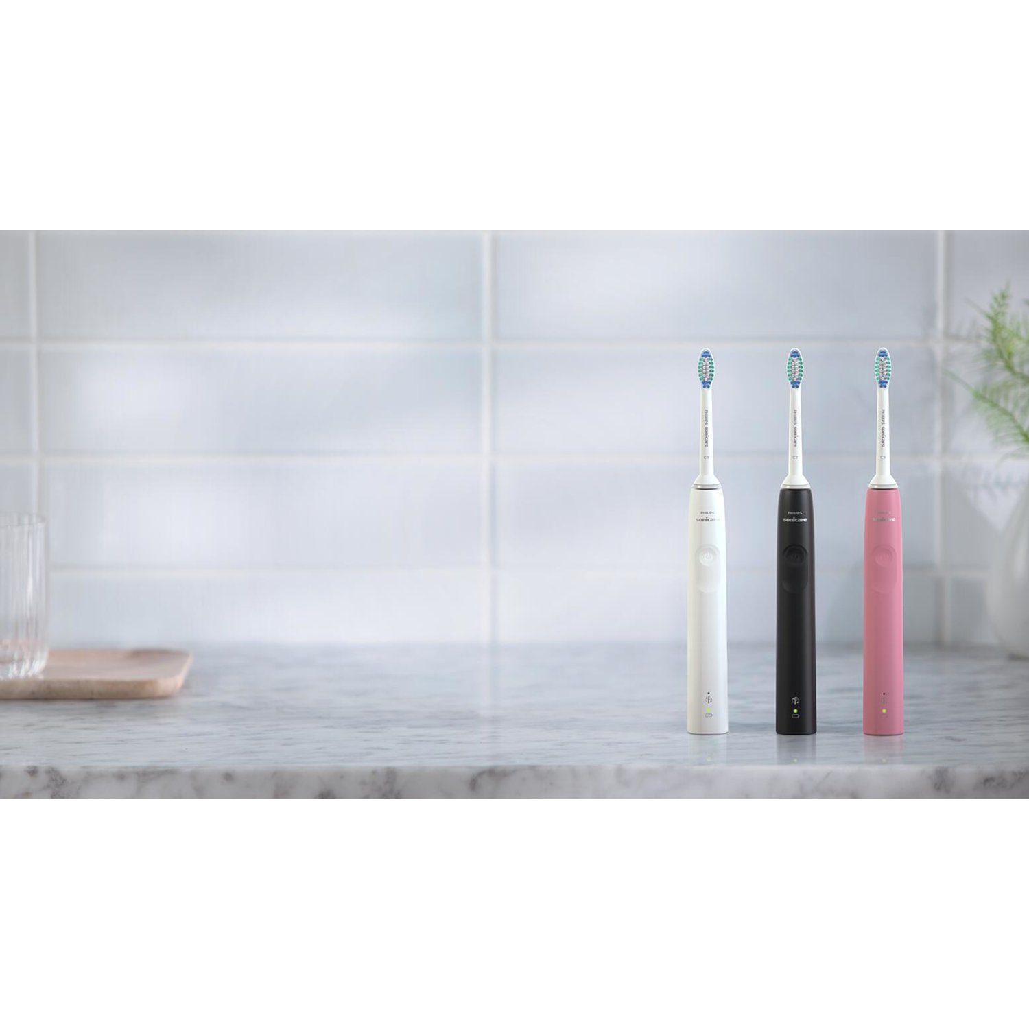 Trzy elektryczne szczoteczki do zębów: biała, czarna i różowa. Ułożone na marmurowym blacie, neutralne tło.