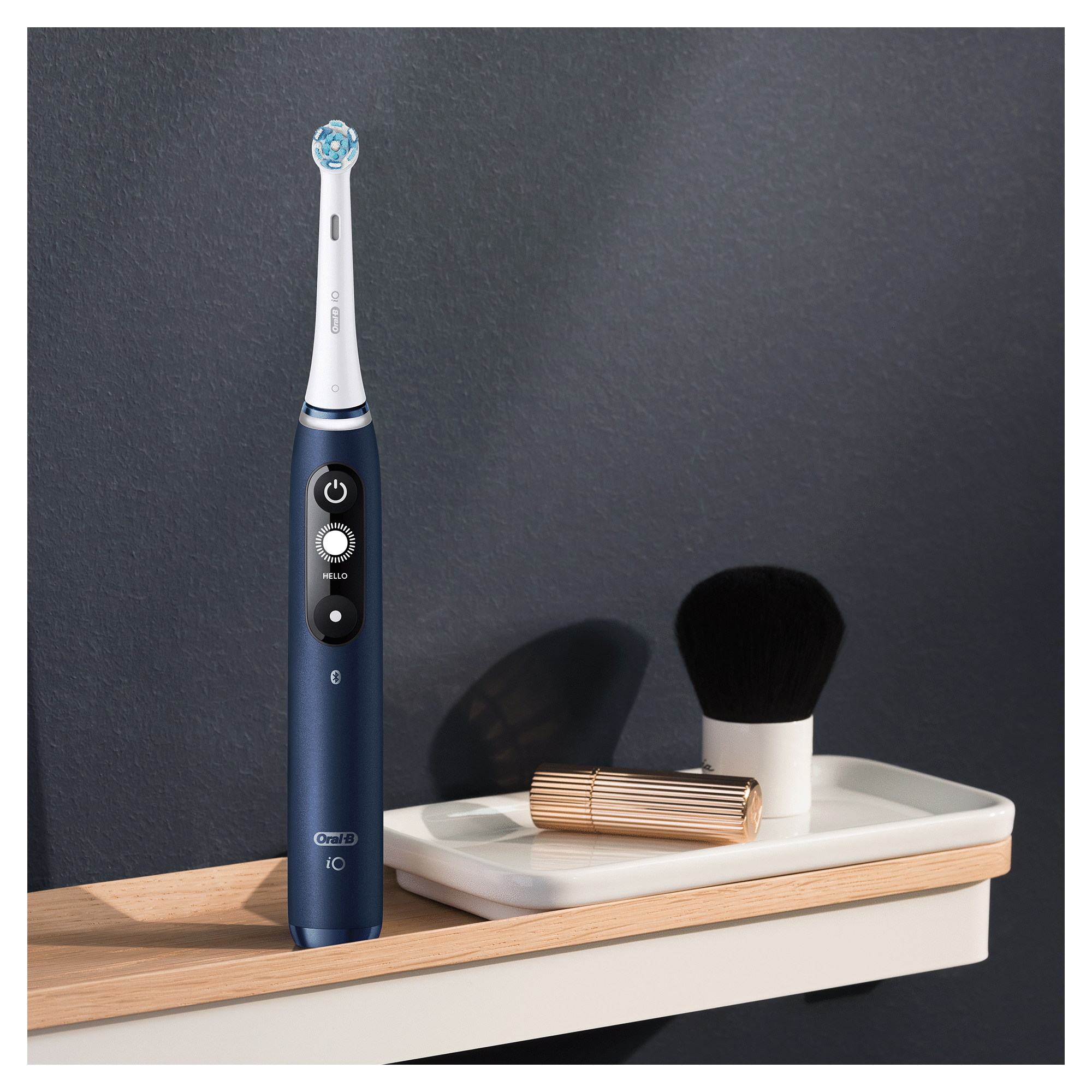 Spazzolino elettrico blu scuro su un vassoio, accanto a un pennello cosmetico e un piccolo contenitore dorato.