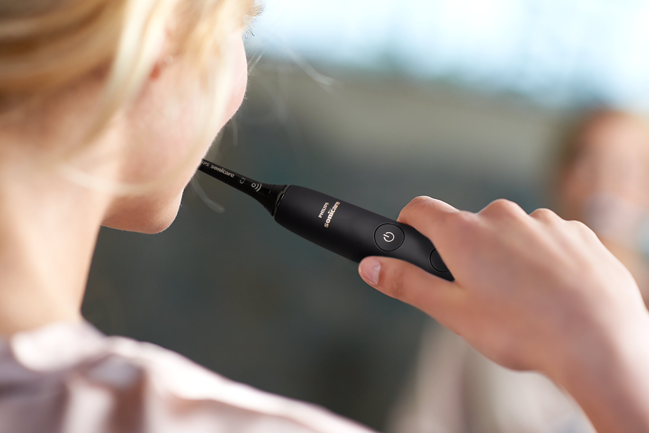 Kobieta myje zęby czarną elektryczną szczoteczką. Rozmyte tło.