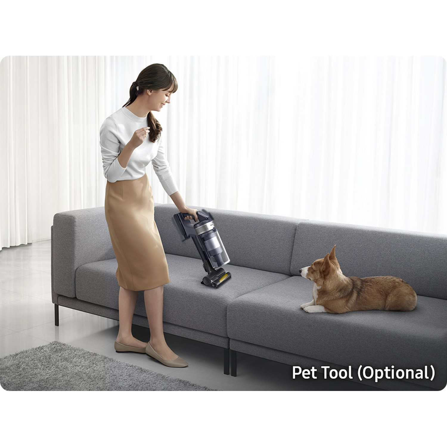 Mujer aspirando el sofá con perro cerca. La aspiradora es negra y plateada.