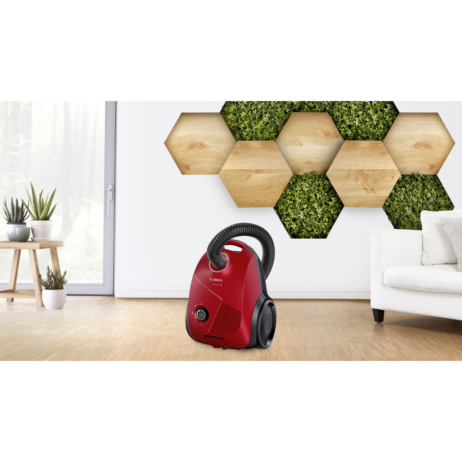 Aspirapolvere rosso in soggiorno moderno con pavimento in legno e decorazioni murali. Piante e divano bianco visibili.