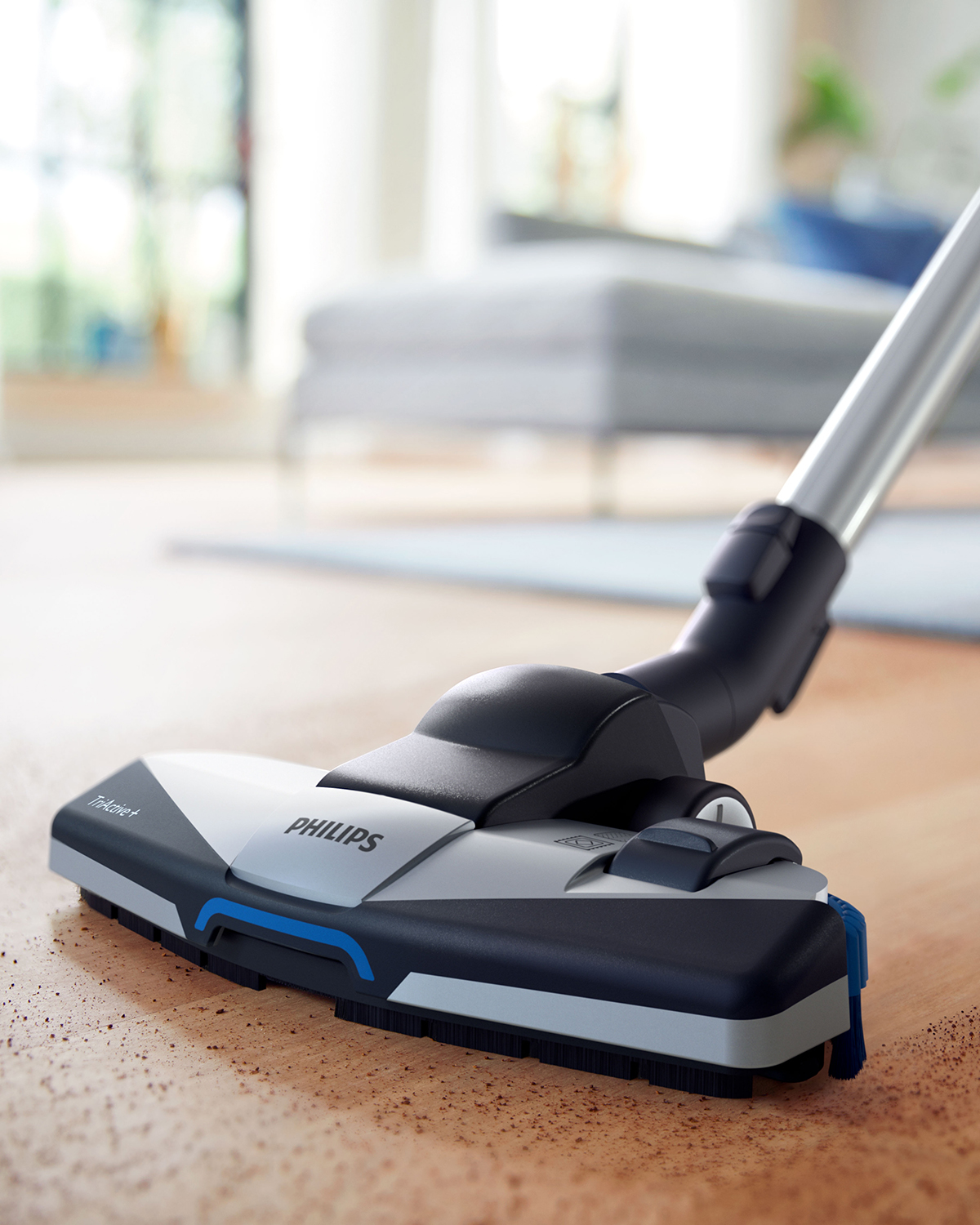 Primo piano della testina dell'aspirapolvere Philips su pavimento in legno. Particelle di polvere visibili.