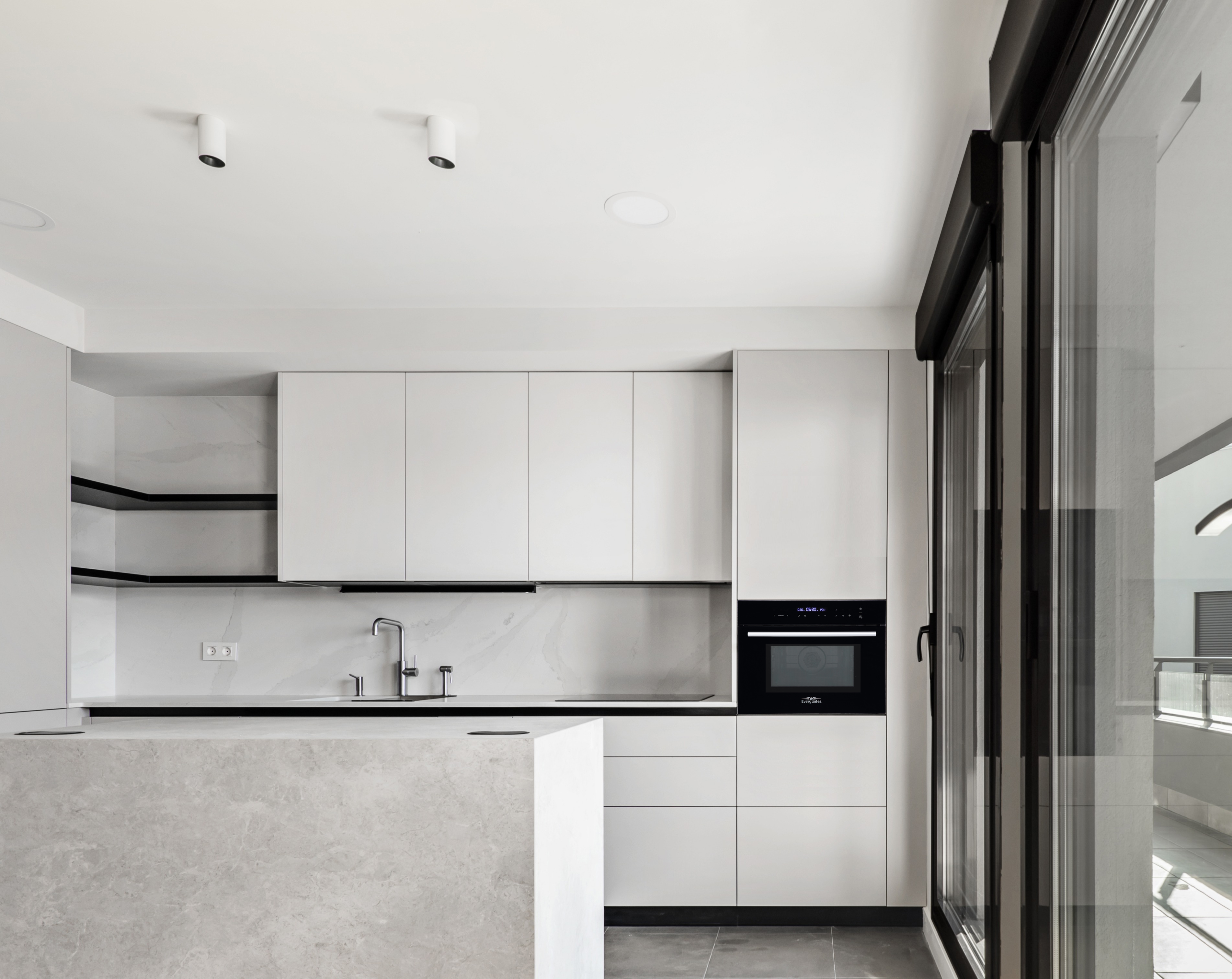 Moderne witte keuken met kasten, eiland, oven en een raam met uitzicht.