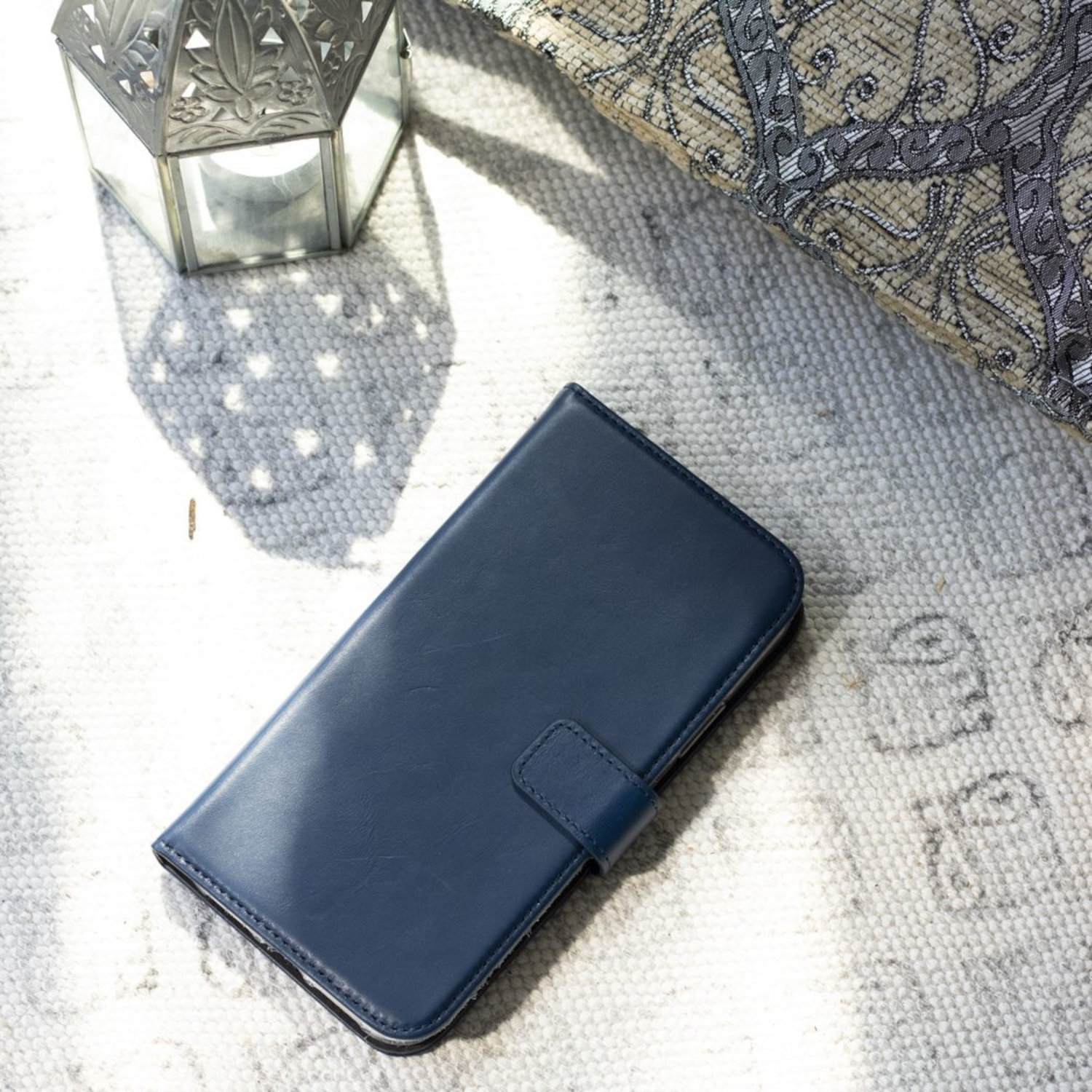 Blauwe telefoonhoes op een patroonkleed, naast een decoratieve lantaarn en een patroon kussen.