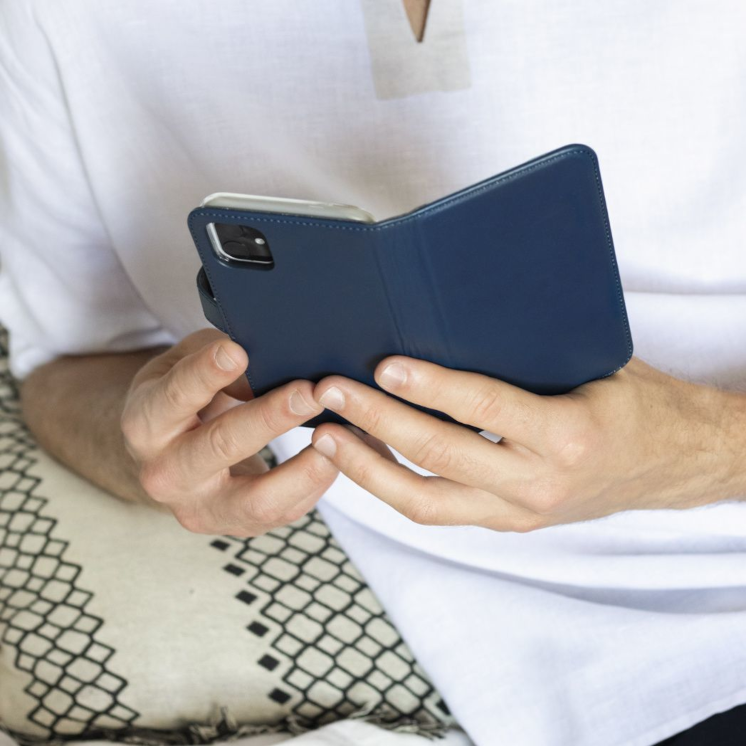 Persoon houdt een blauwe telefoonhoes met een telefoon erin vast, op een witte en beige achtergrond.
