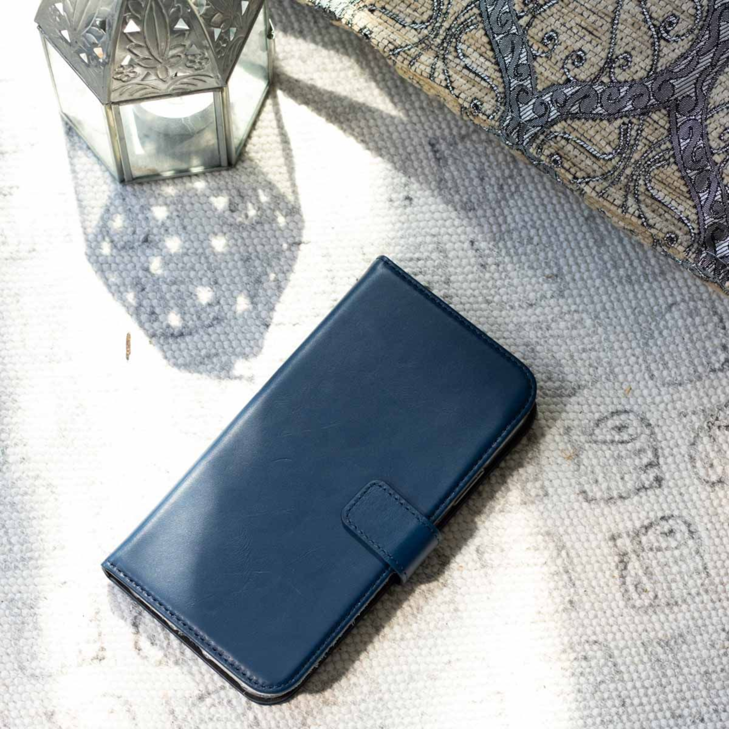 Blauwe telefoonhoes op een kleed. De hoes is open, onthult het scherm van de telefoon. Zonnig licht.