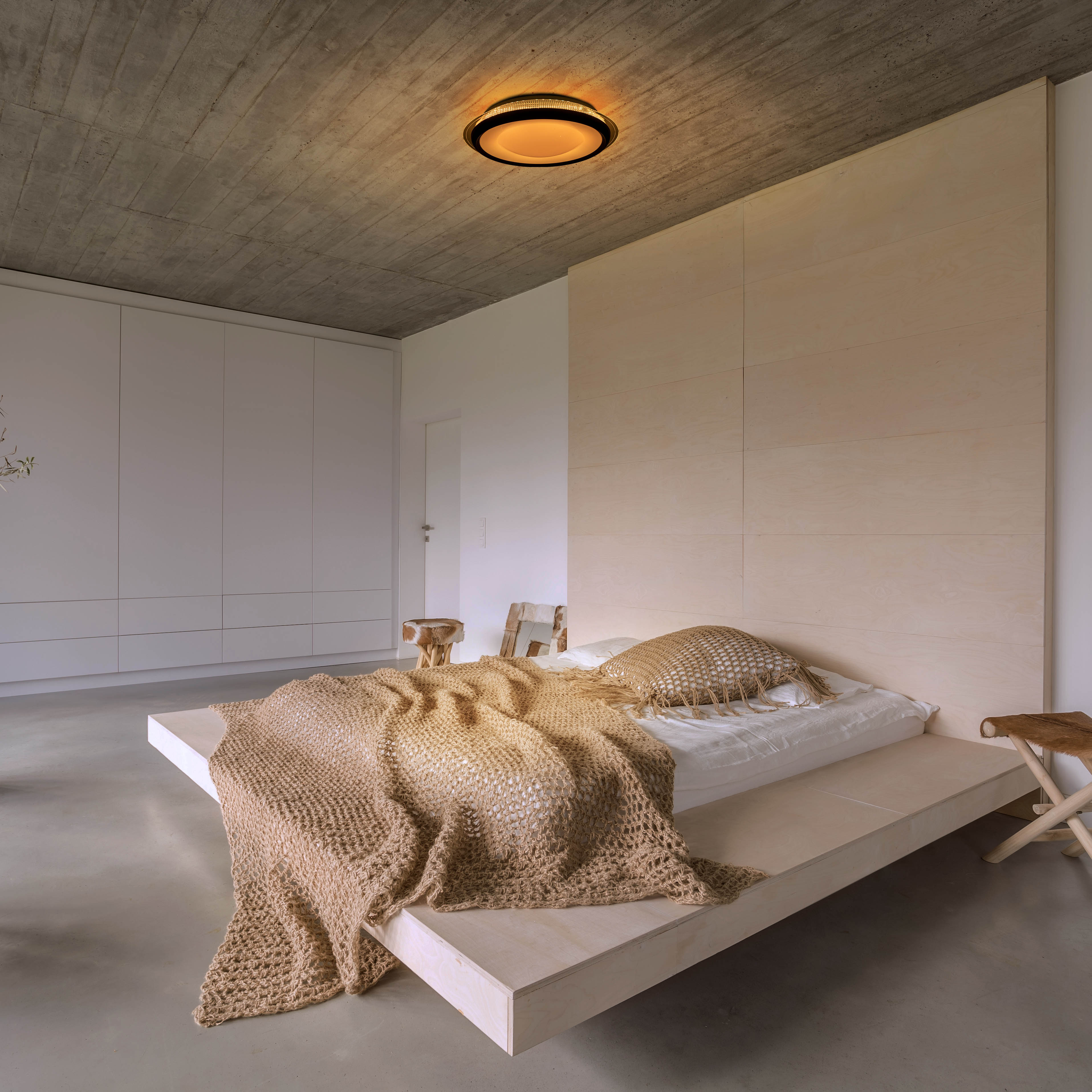 Schlafzimmer mit Bett auf Podest, Holz-Kopfteil und Betondecke.