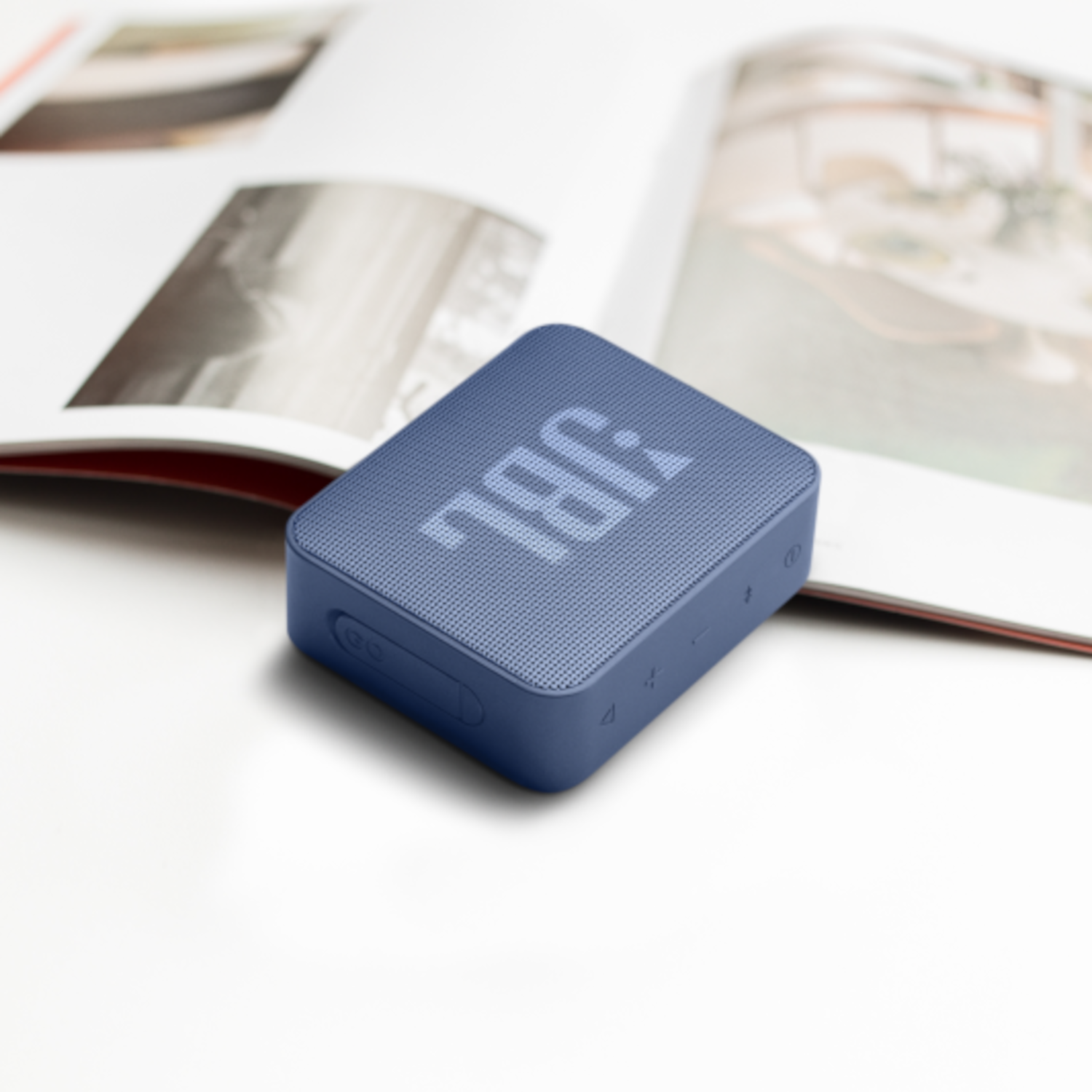 Niebieski kwadratowy głośnik JBL na białej powierzchni z otwartym magazynem.