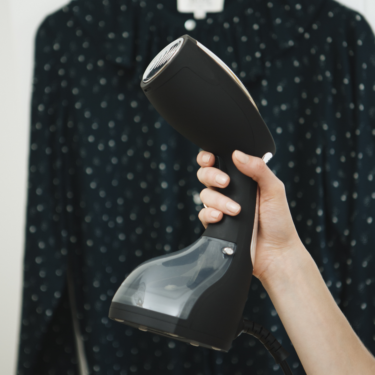 Hand die een zwarte kledingstomer boven een overhemd houdt.