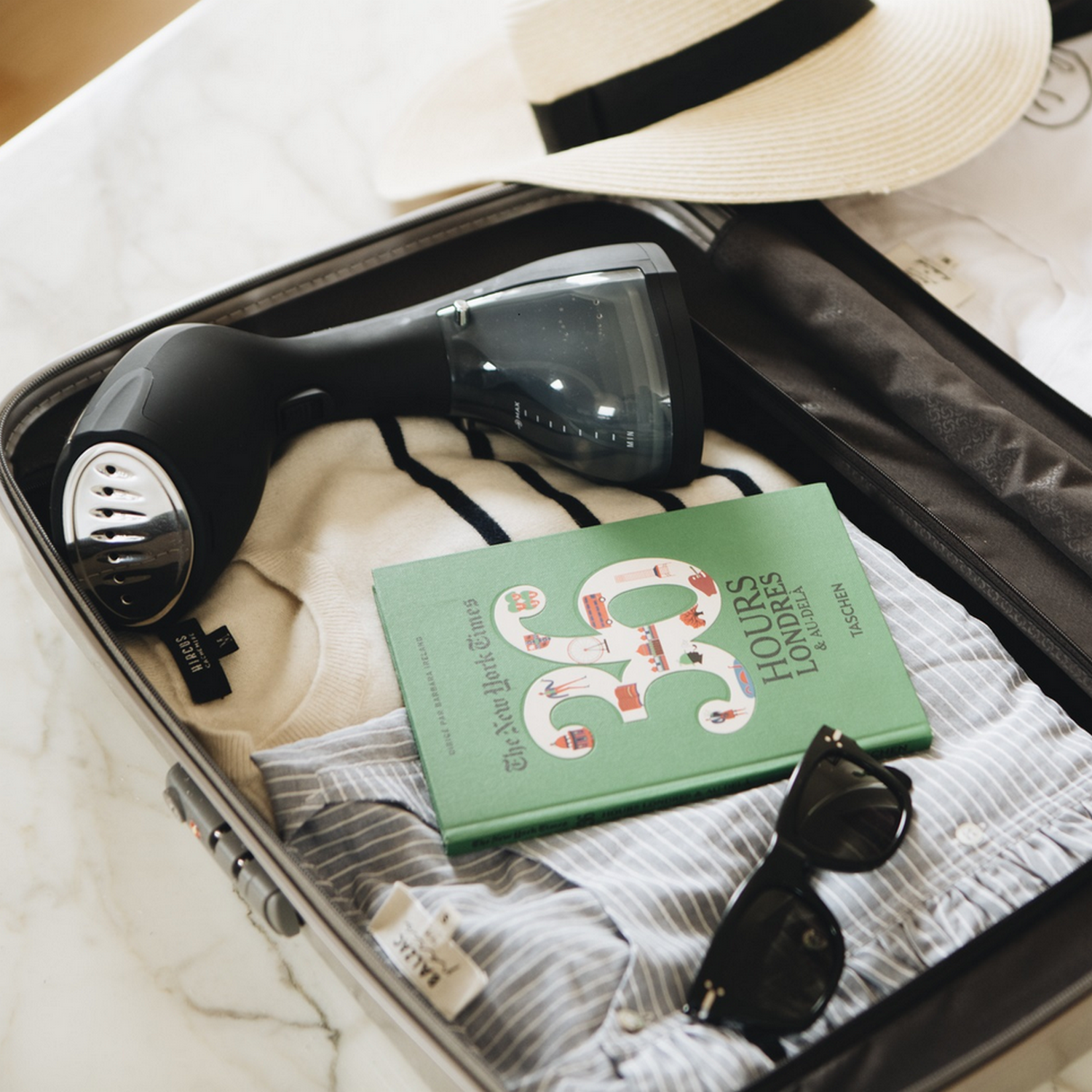 Open koffer, met kleding, boek, zonnebril en een stomer.