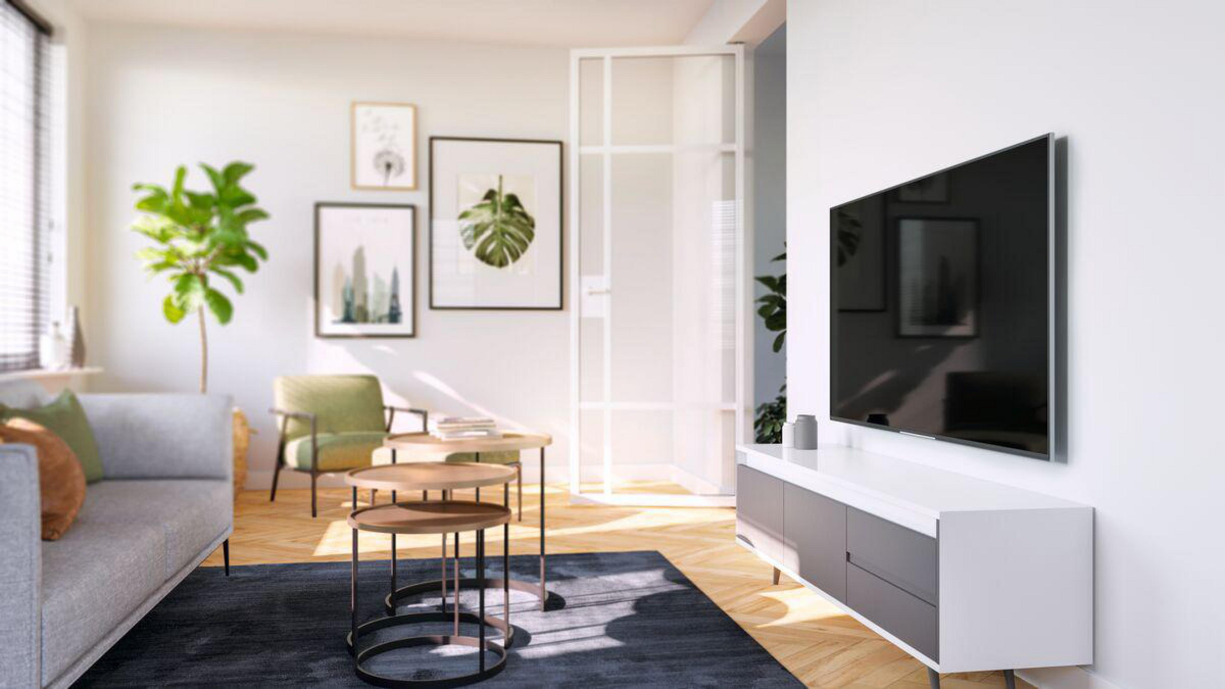 Salon z telewizorem na ścianie i szarą sofą. Są oprawione obrazy i dywan.