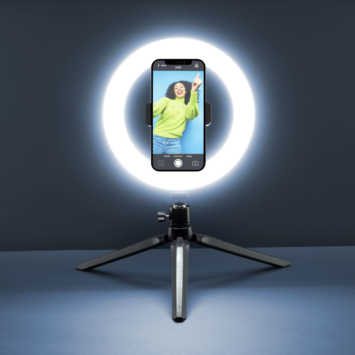 Un telefono con una donna davanti a una luce ad anello su un treppiede.