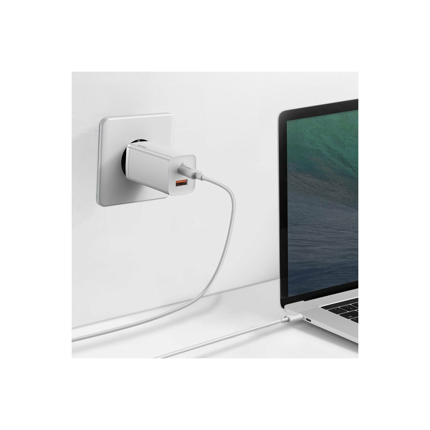 Biała ładowarka podłączona do gniazdka ściennego i laptop z podłączonym białym kablem.