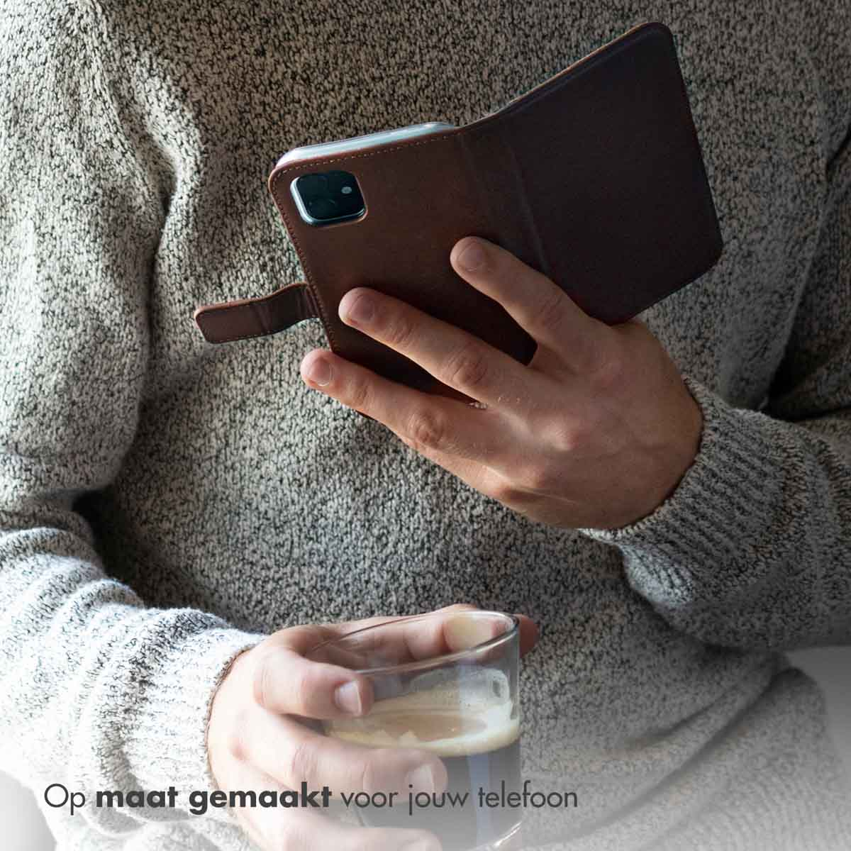 Eine Person hält eine braune Leder-Handyhülle mit einem Telefon darin. Die Person hält ein Glas.