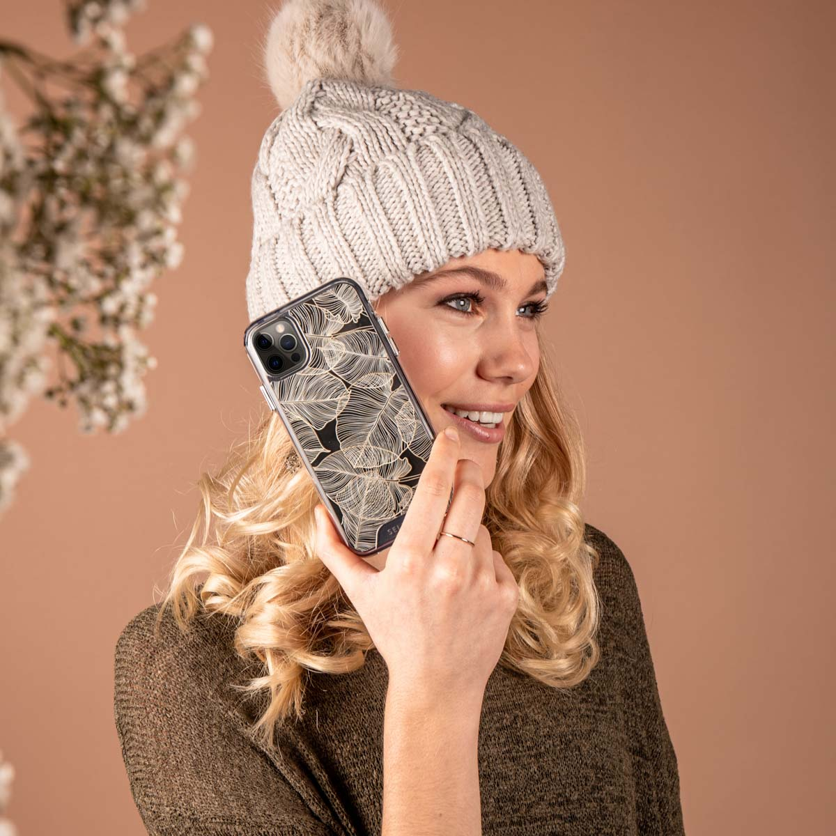 Vrouw houdt een telefoon met hoesje vast. Ze draagt een muts en een groene trui.