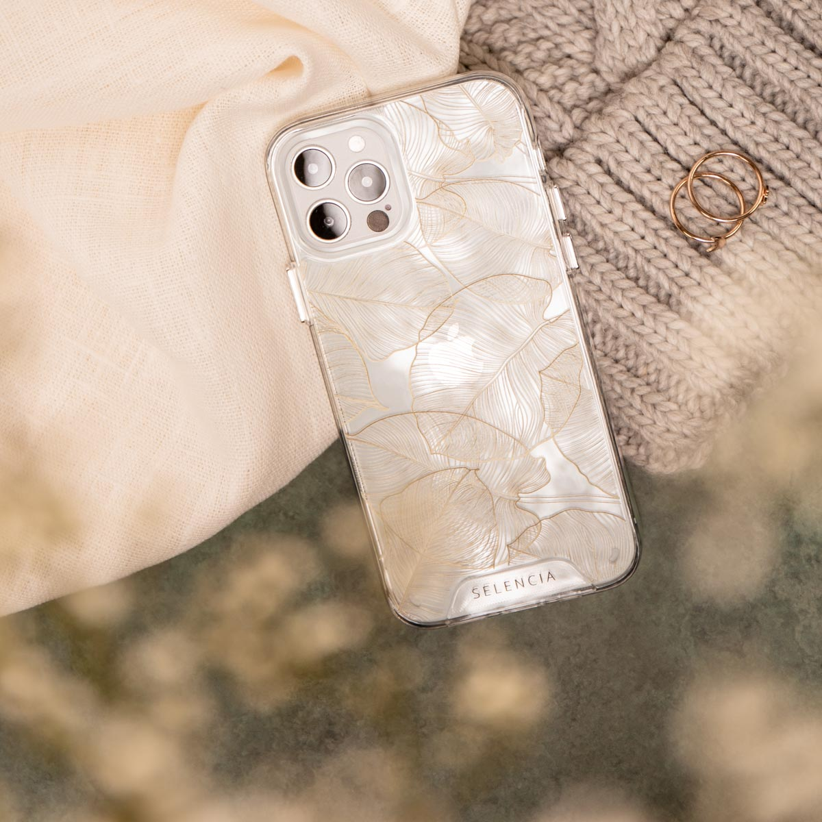 Telefoonhoesje met bloemenontwerp op een beige oppervlak met stof en ringen.