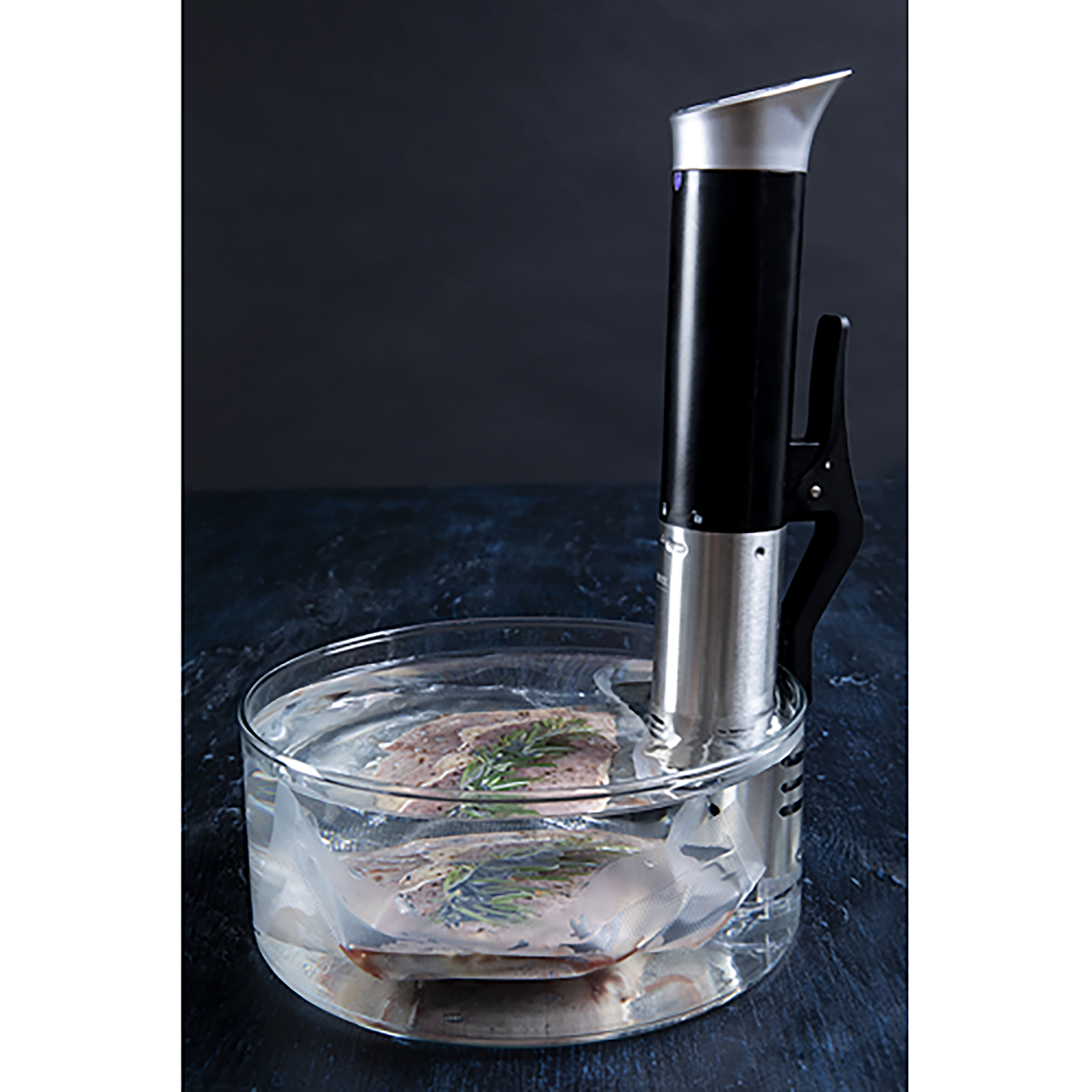 Een sous vide kooktoestel in een glazen bak met voedsel in een zak, in een donkere omgeving.