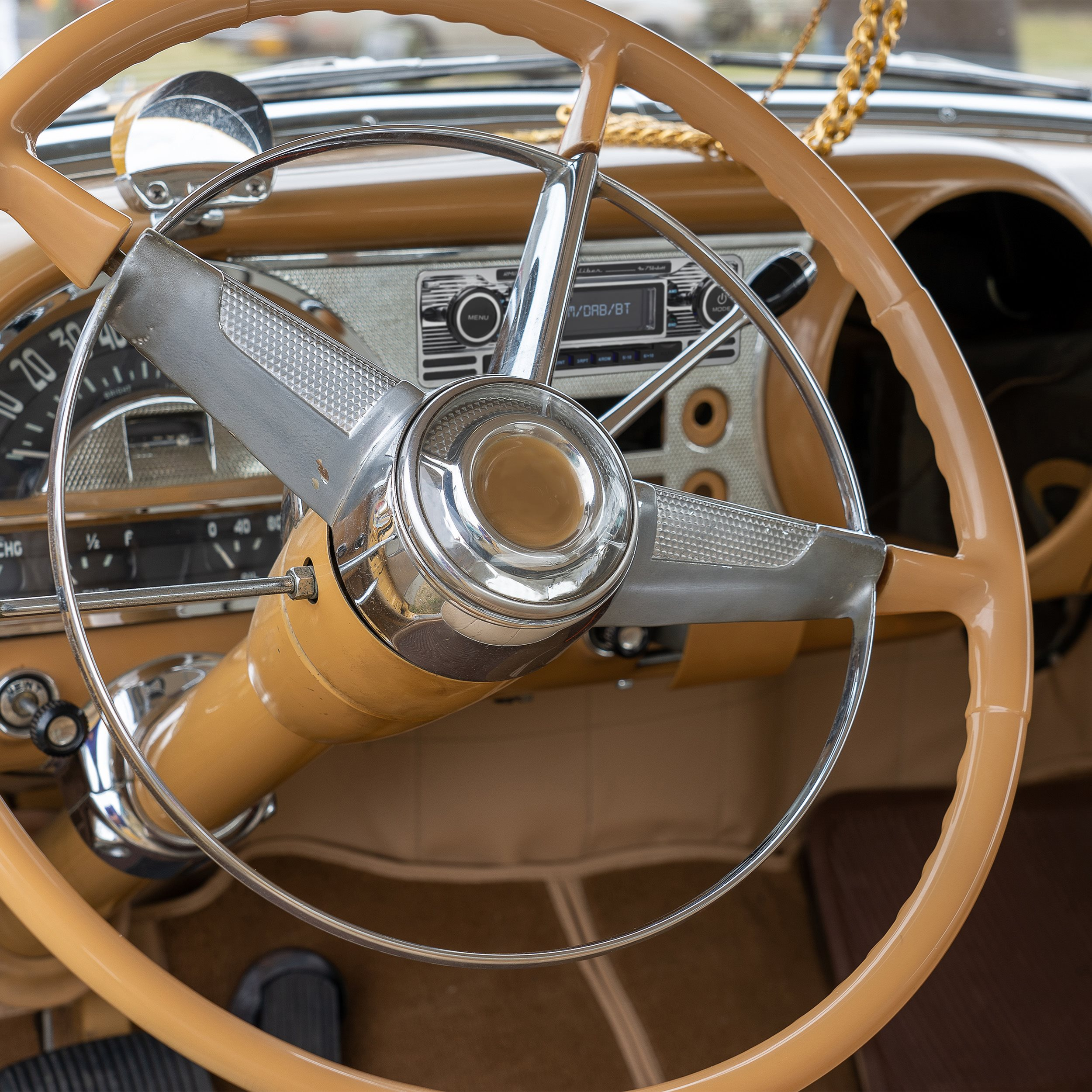 Close-up of a car steering wheel. The steering wheel is tan colored and has a chrome center.