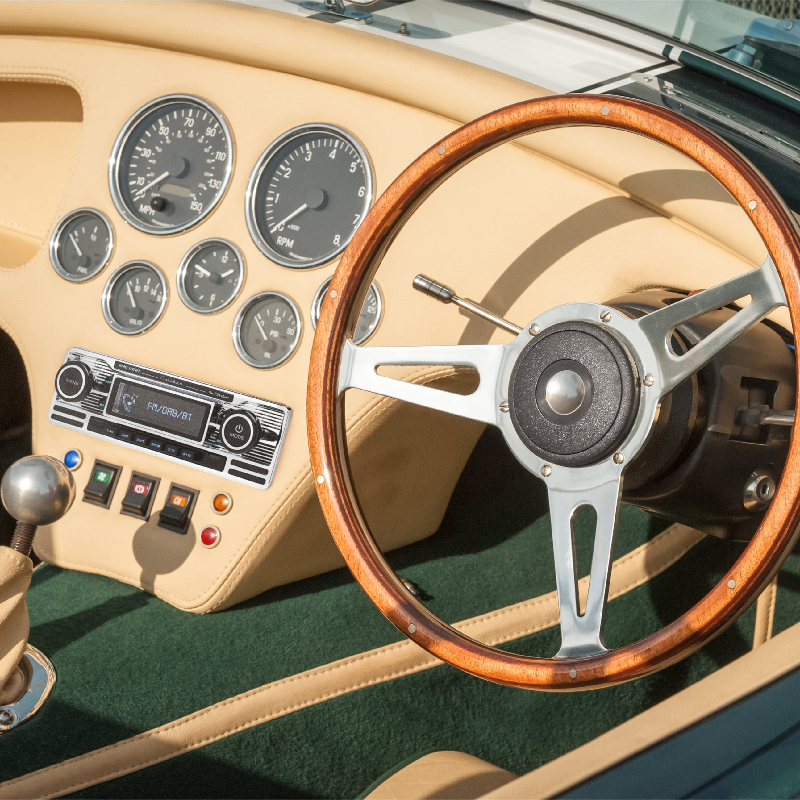Classic car dashboard. Wood steering wheel, gauges, radio, and beige interior.