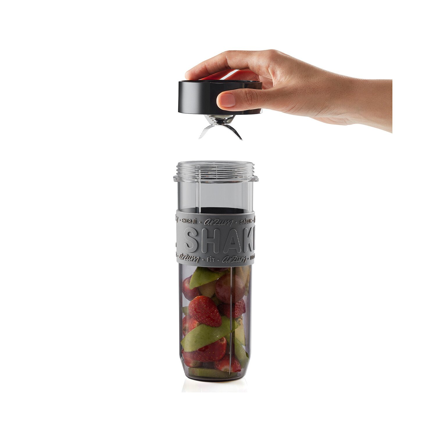 Hand hält Blender-Oberteil über Glas mit Früchten. Weißer Hintergrund.