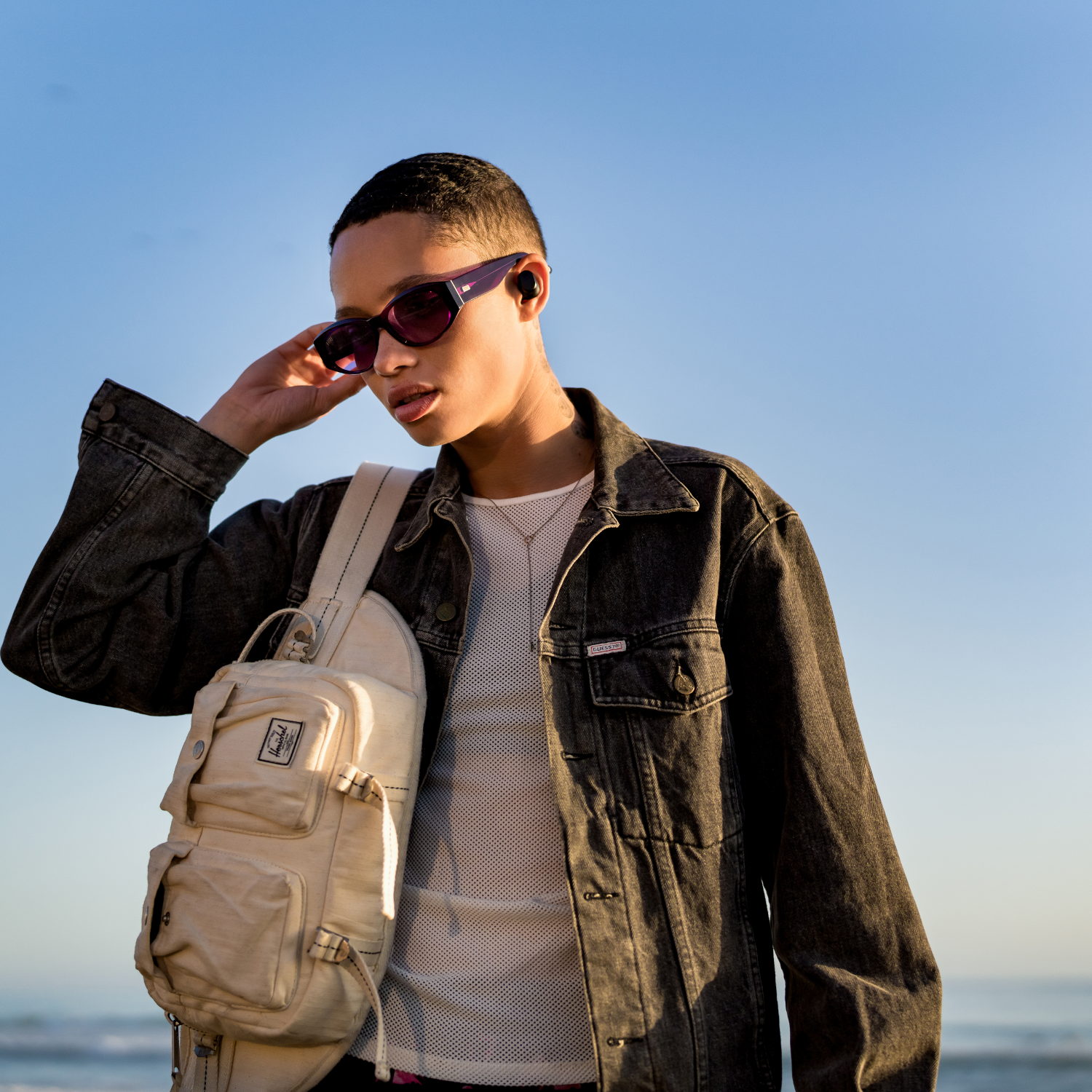 Person trägt Sonnenbrille und Tasche, mit Ohrhörern in den Ohren.