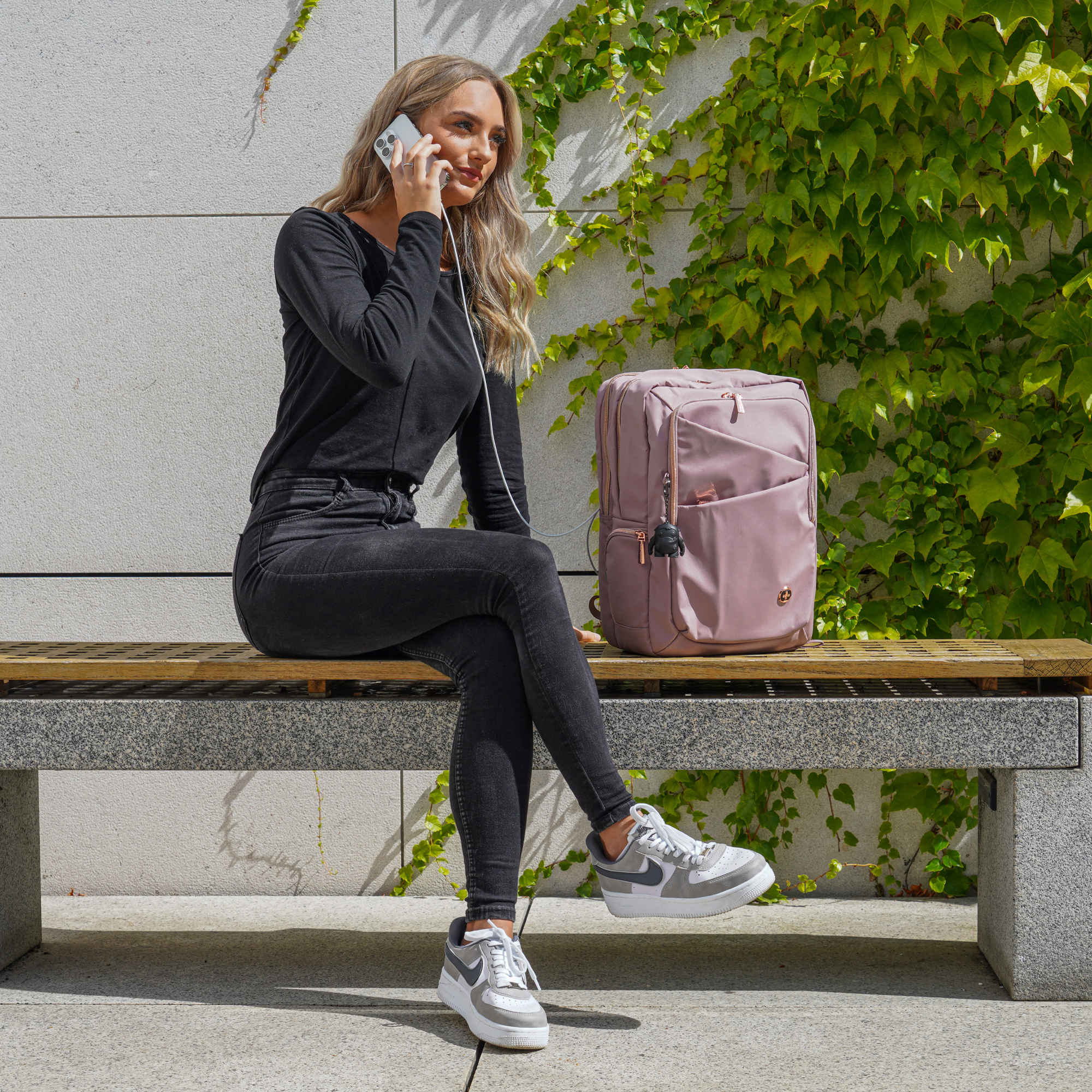 Donna su una panchina che parla al telefono, con uno zaino rosa.
