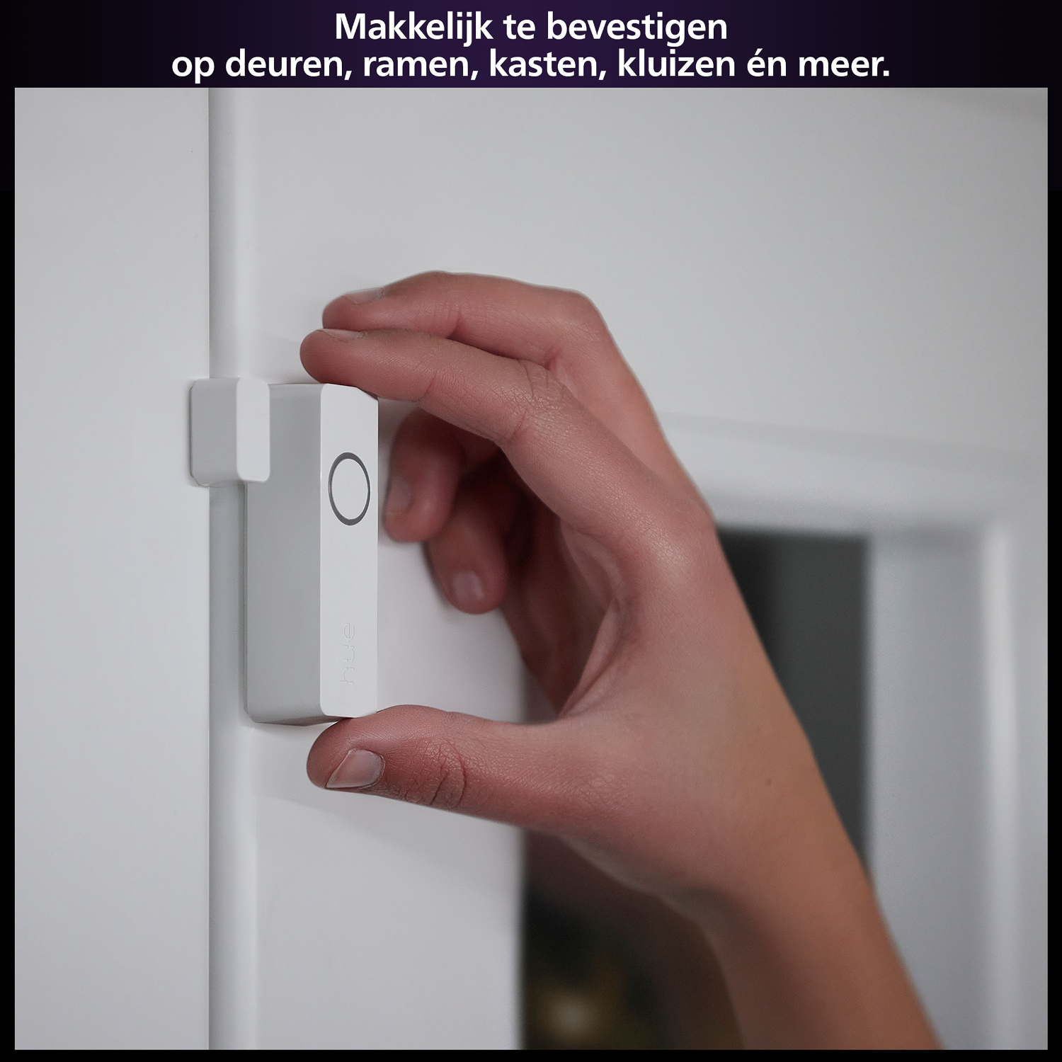 Dłoń trzymająca białe urządzenie smart home obok białej ramy drzwi.