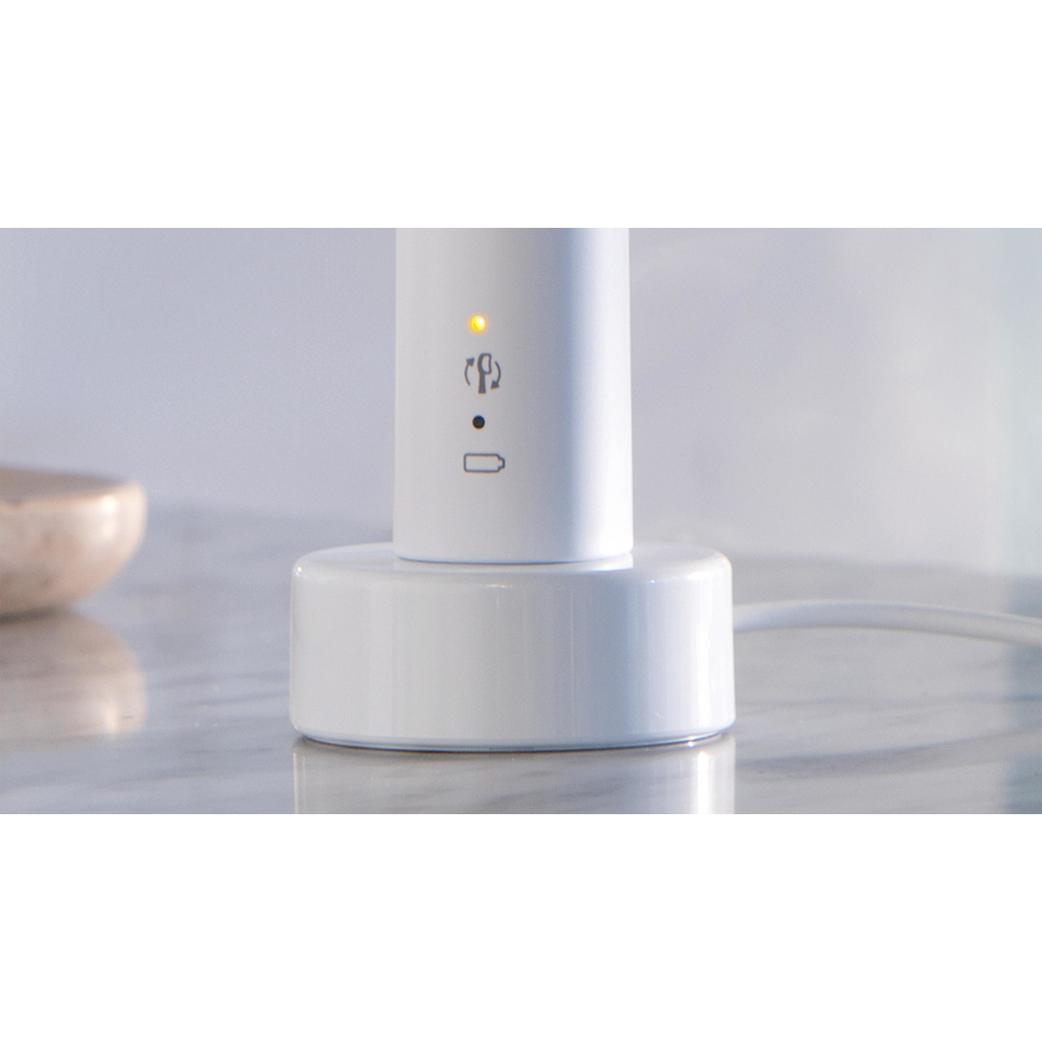 Biała szczoteczka do zębów ładująca się na białej podstawie, ze wskaźnikiem. Marmurowa powierzchnia.