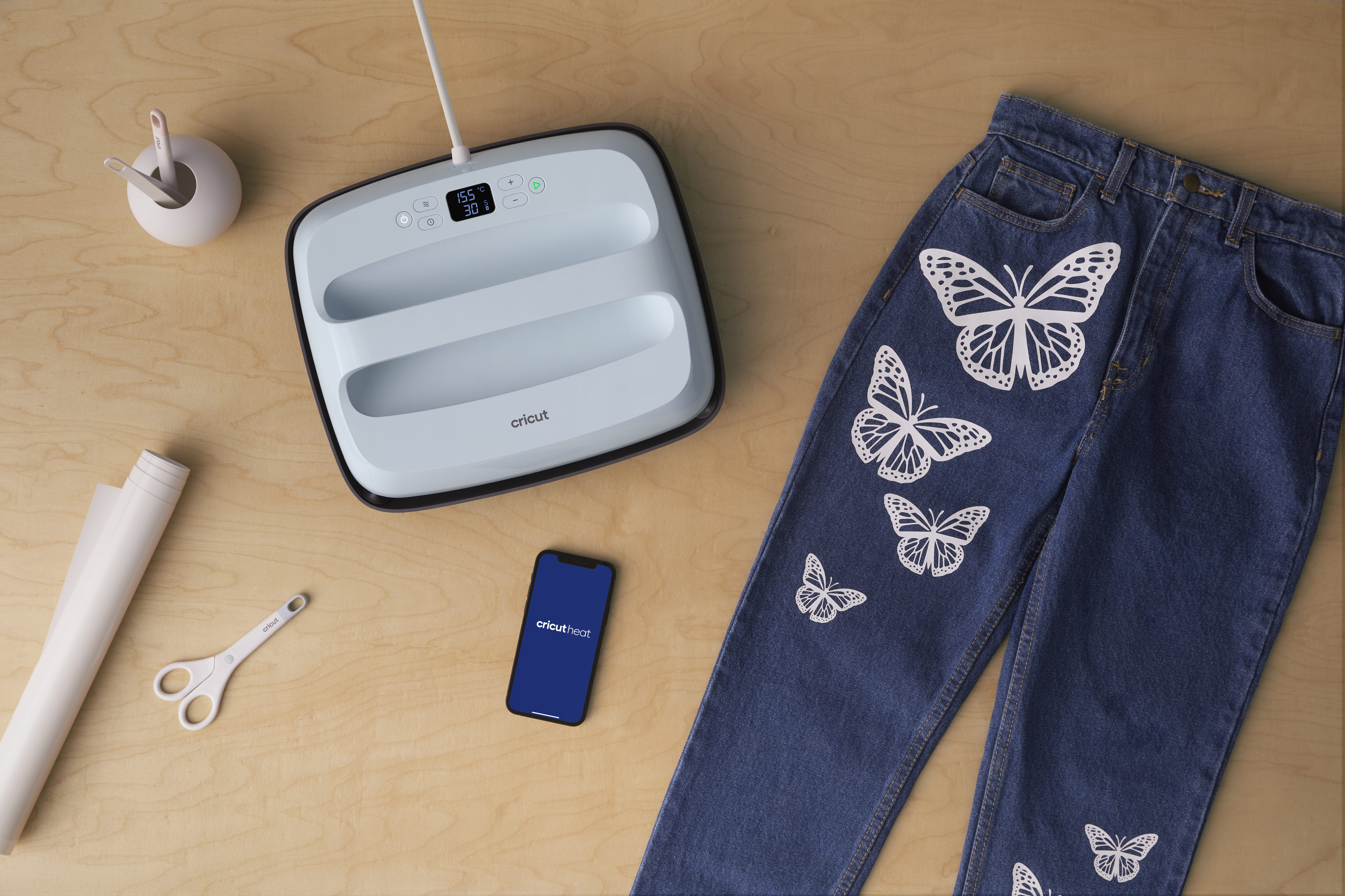 Una pressa a caldo, jeans con farfalle, telefono e materiali per hobby su tavolo in legno.
