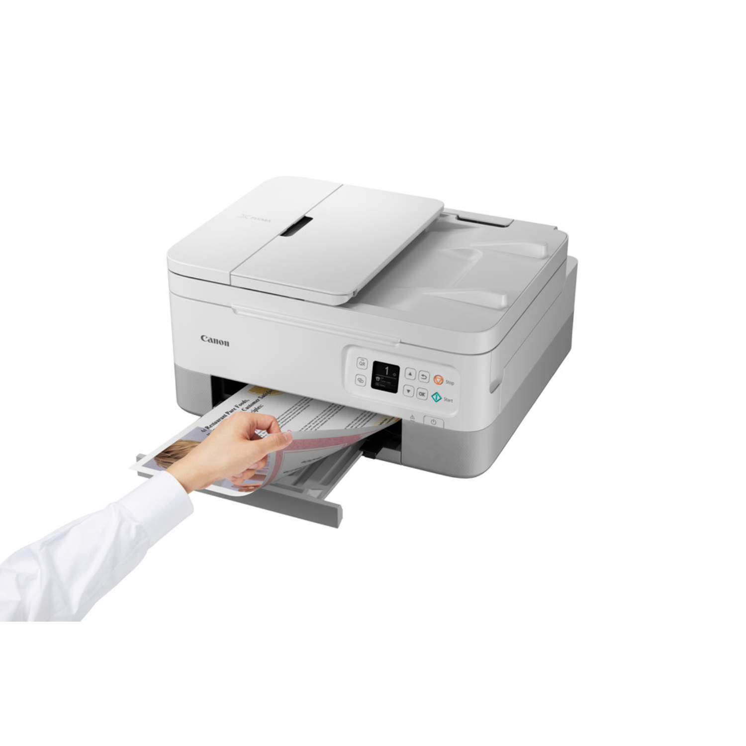 Biała drukarka Canon. Osoba wyciąga kartkę papieru z podajnika wyjściowego.