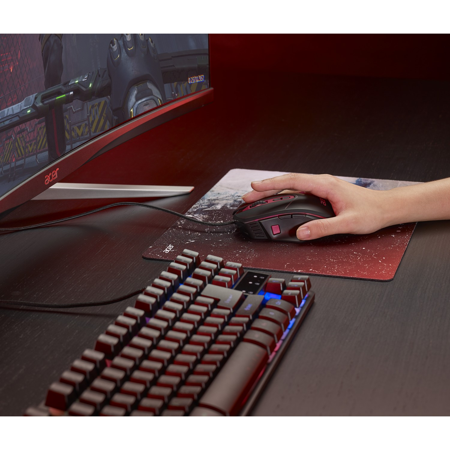 Una mano su un mouse da gaming nero su un tappetino, con tastiera e monitor che mostra un gioco.