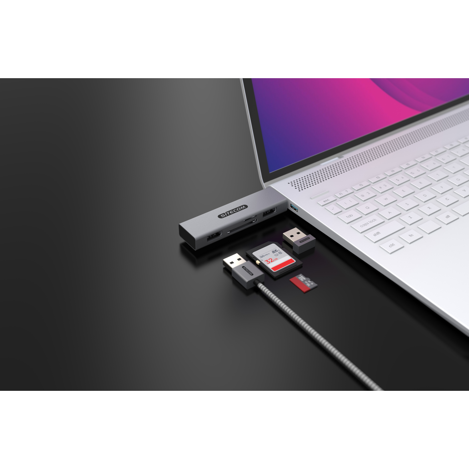 Laptop mit mehreren Adaptern und Geräten verbunden. Dunkler Hintergrund.