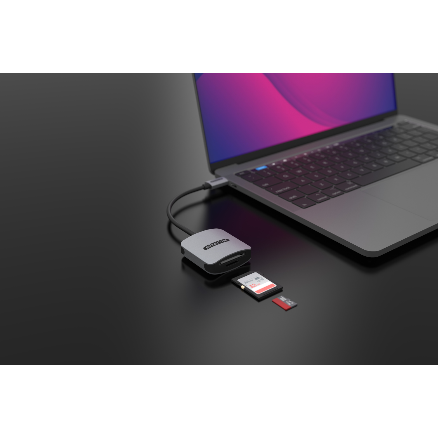 Adattatore Sitecom grigio con schede SD e MicroSD, collegato a un laptop su una superficie nera.
