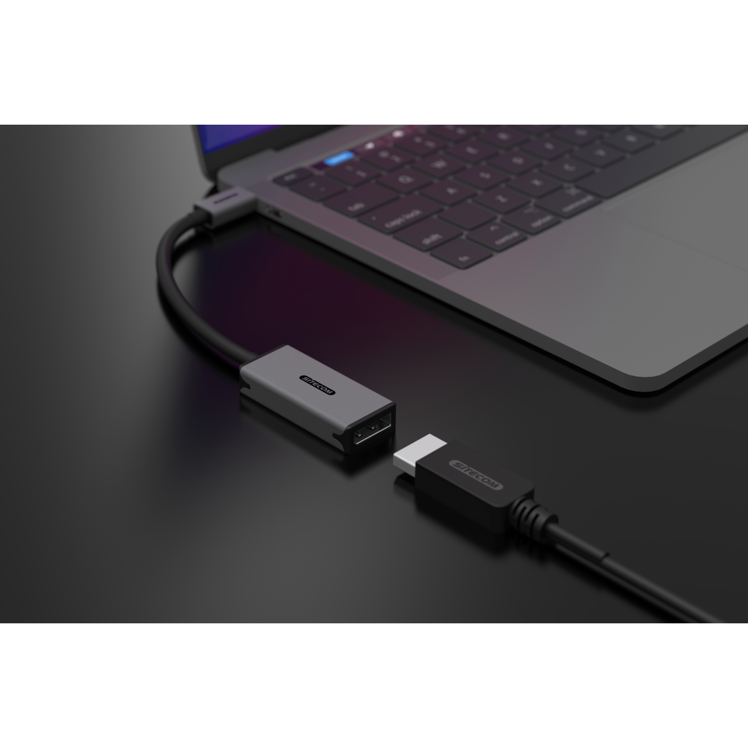 Adattatore Sitecom grigio collegato a un laptop e un cavo HDMI, su superficie nera.