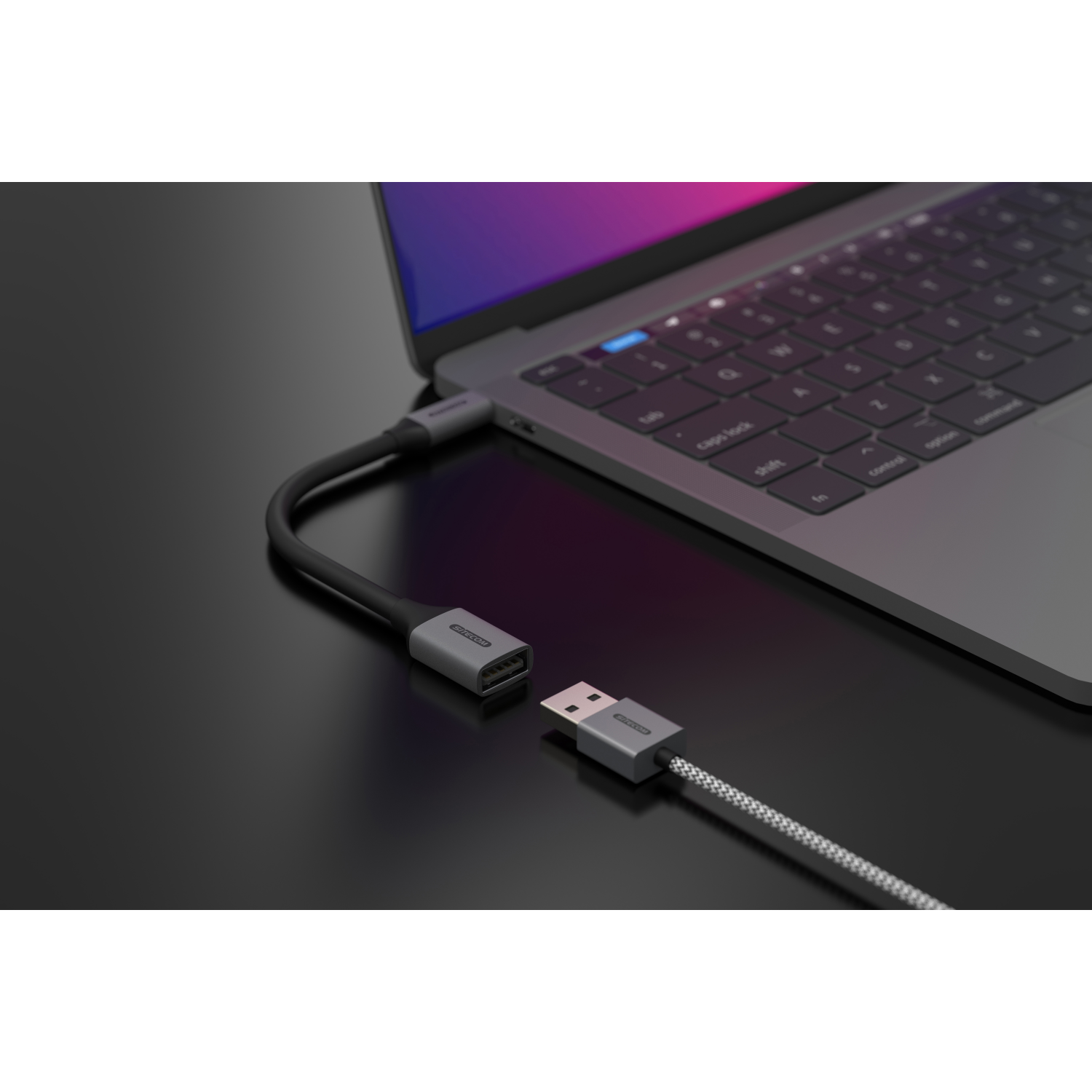 Grauer Adapter verbindet sich mit Laptop, USB-Kabel angeschlossen, auf schwarzer Oberfläche.