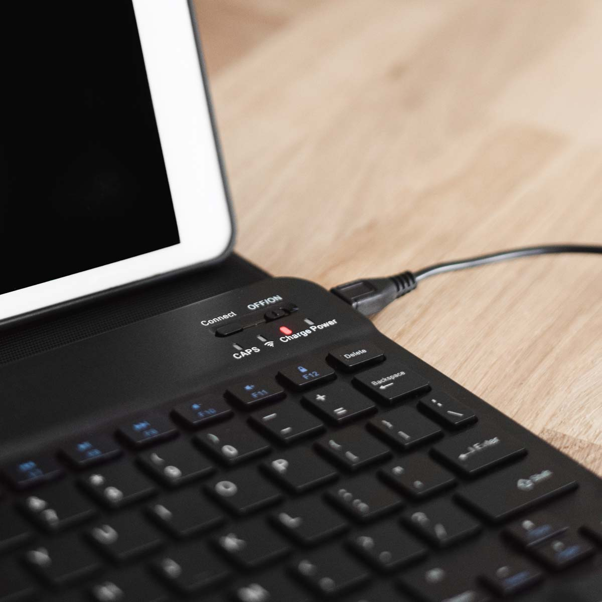 Zwart toetsenbord aangesloten op een tablet. Het toetsenbord staat op een houten oppervlak.