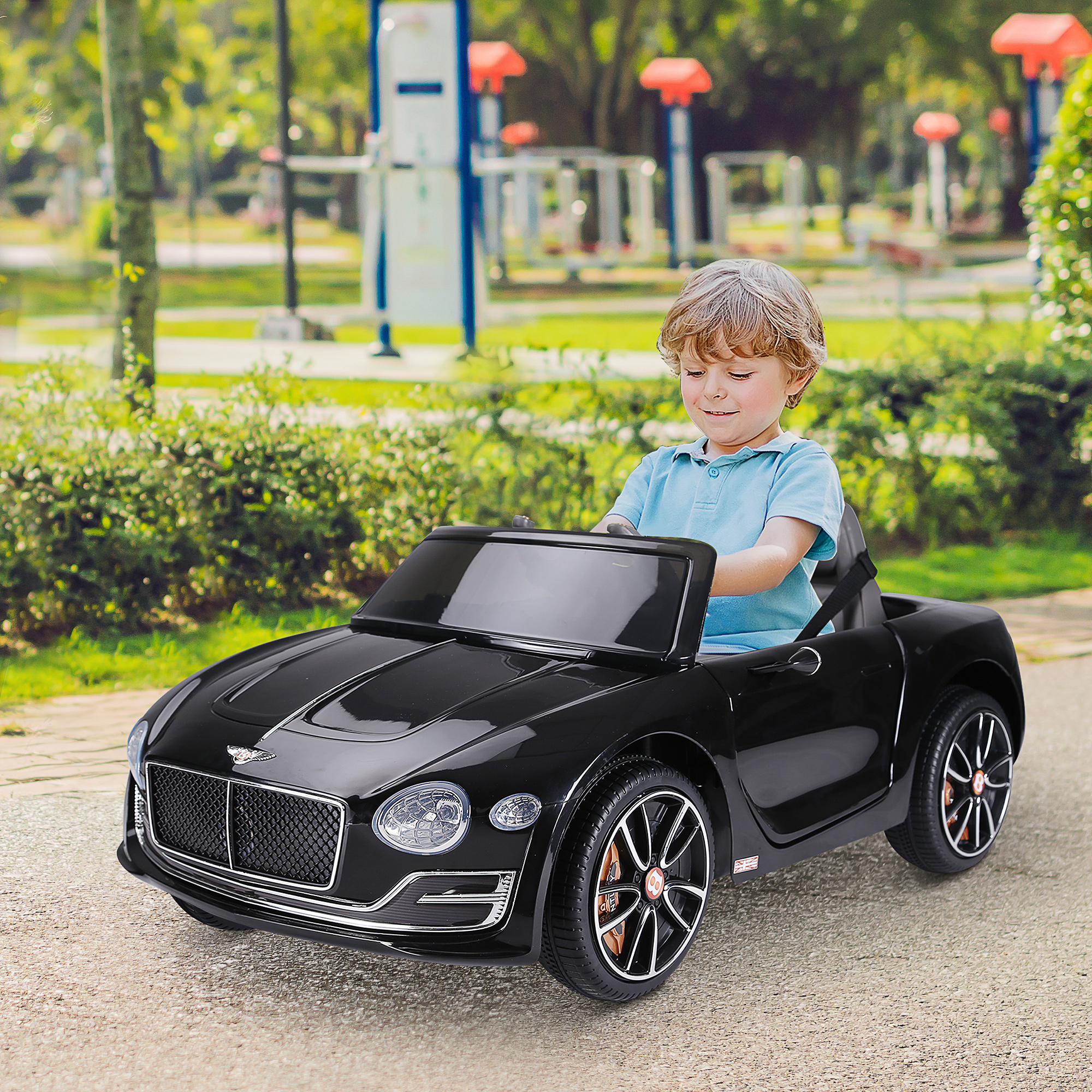 Un niño pequeño sentado en un coche de juguete negro sobre un camino pavimentado. El coche es descapotable.