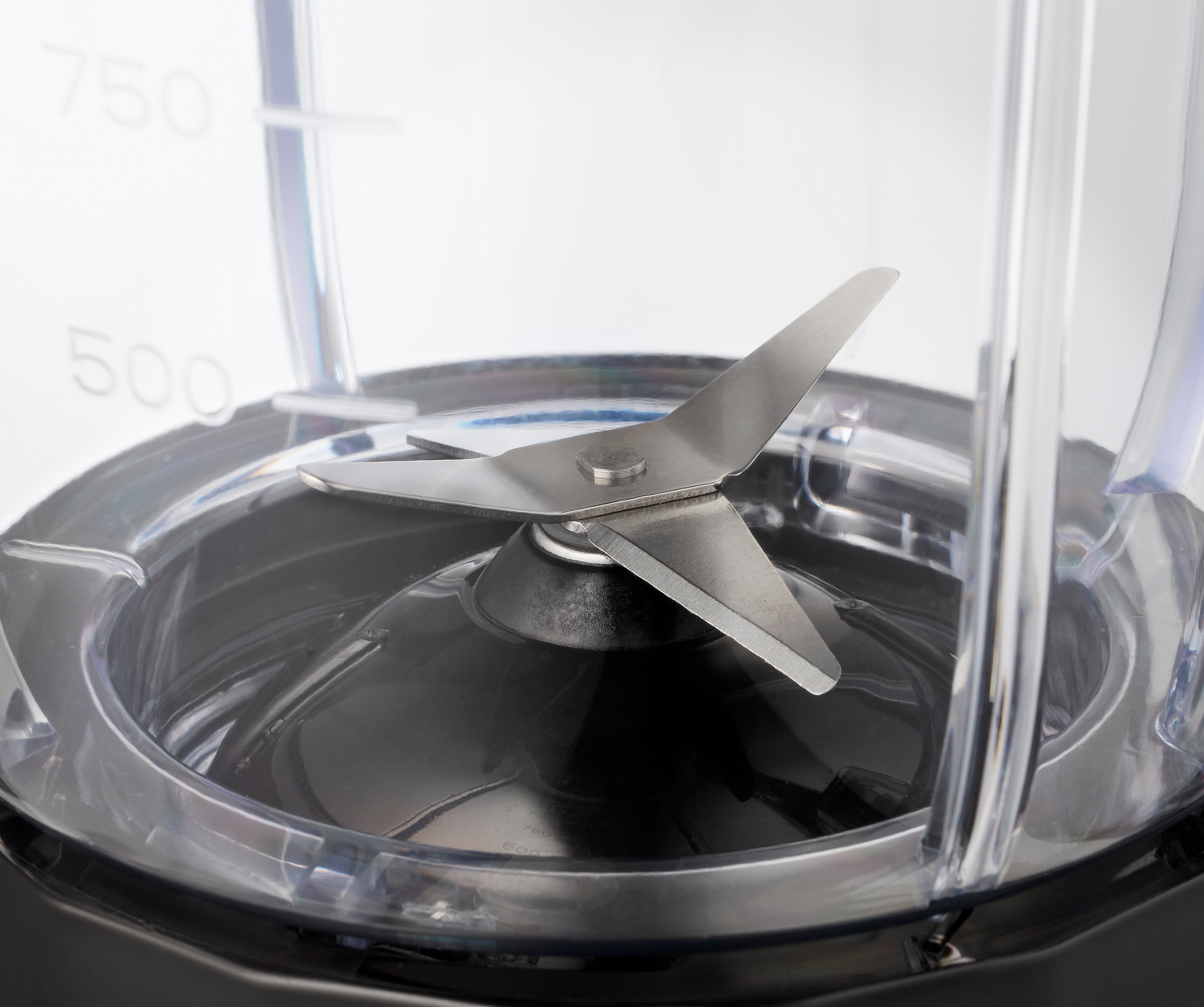 Close-up of a blender blade assembly. The blade is in the center of a transparent container.