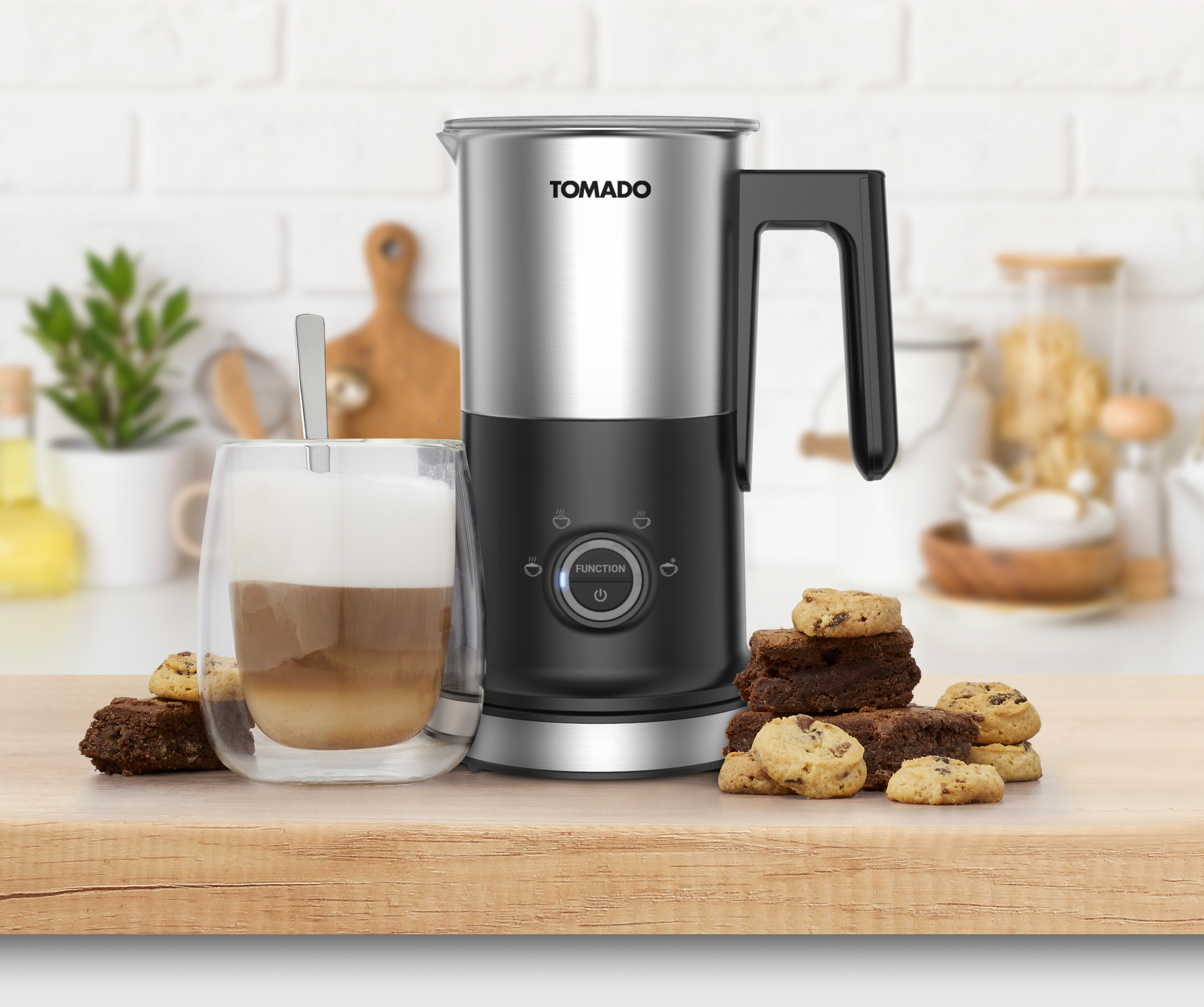 Melkopschuimer, glas latte, koekjes en brownies op hout. Keuken met planten.