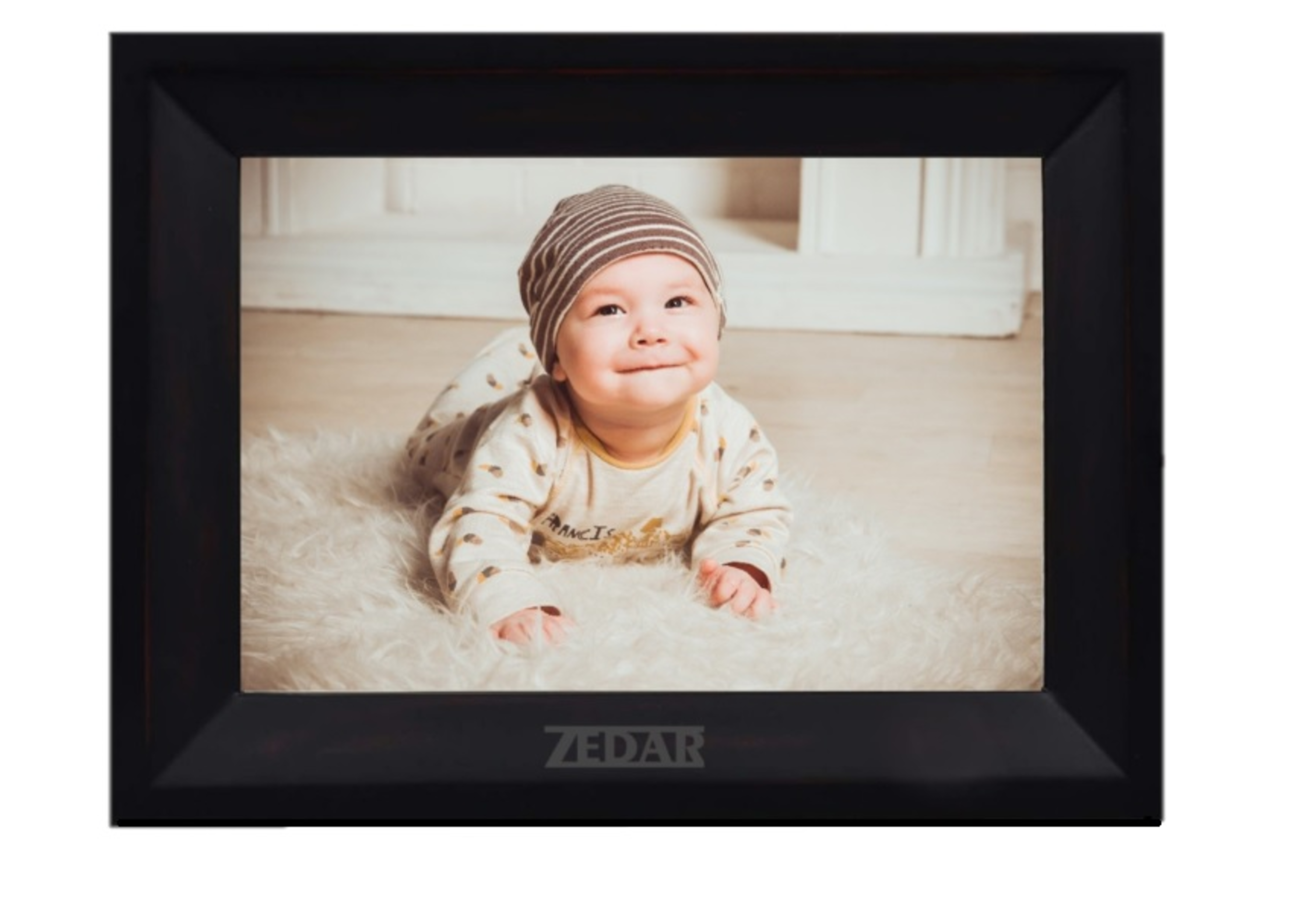 A baby wearing a hat and onesie smiles while lying on a white fluffy rug in a frame.