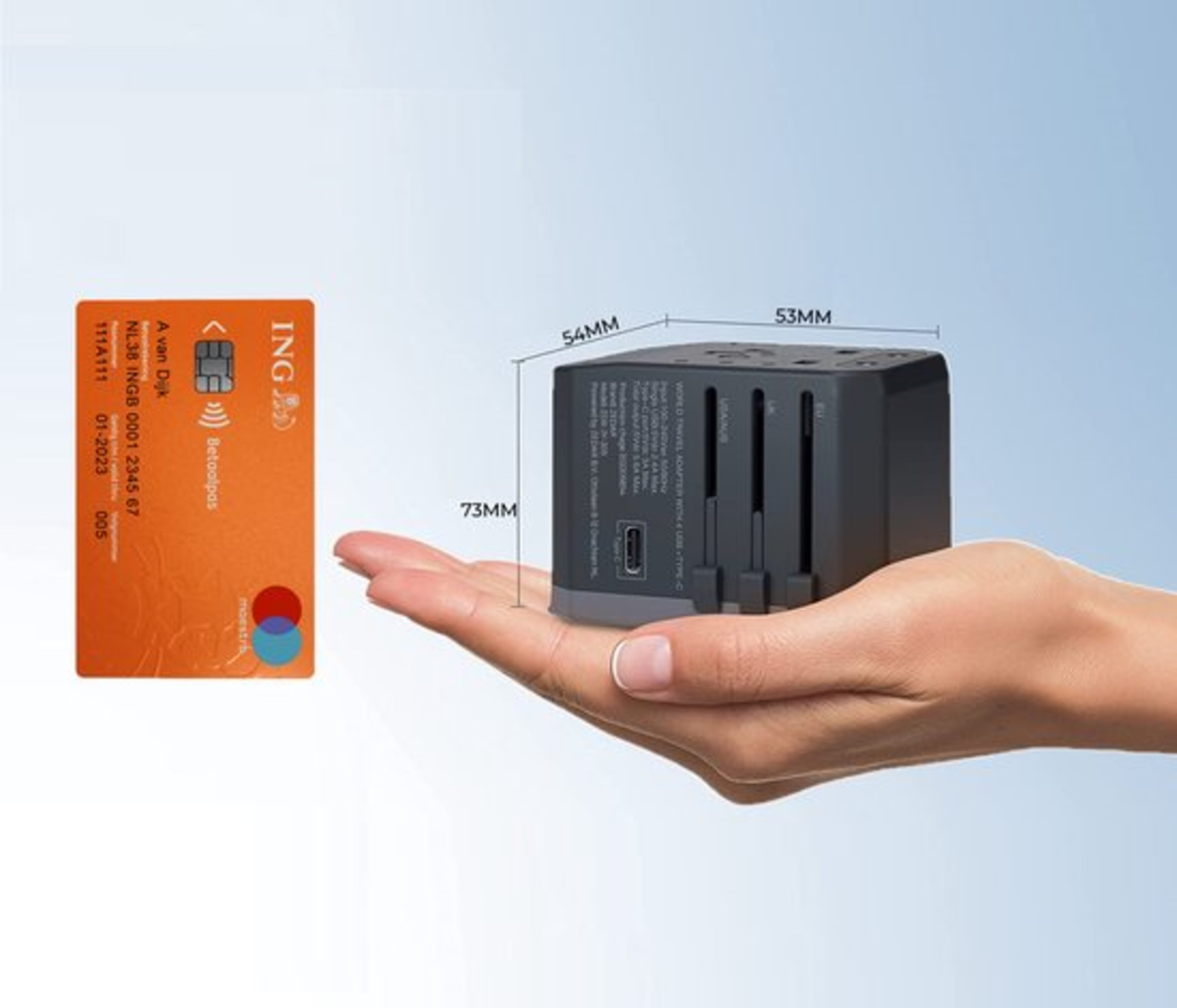 Hand holding a travel adapter with dimensions and a credit card. Neutral background.
