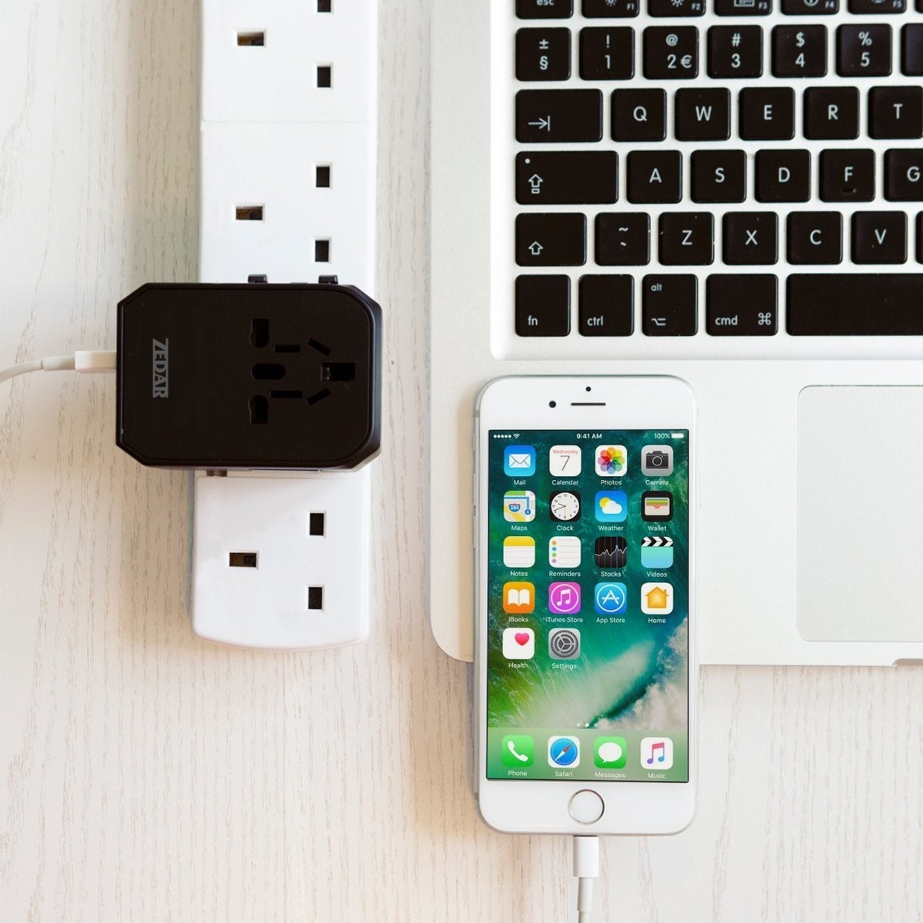 Laptop, phone charging, and adapter on a white table.